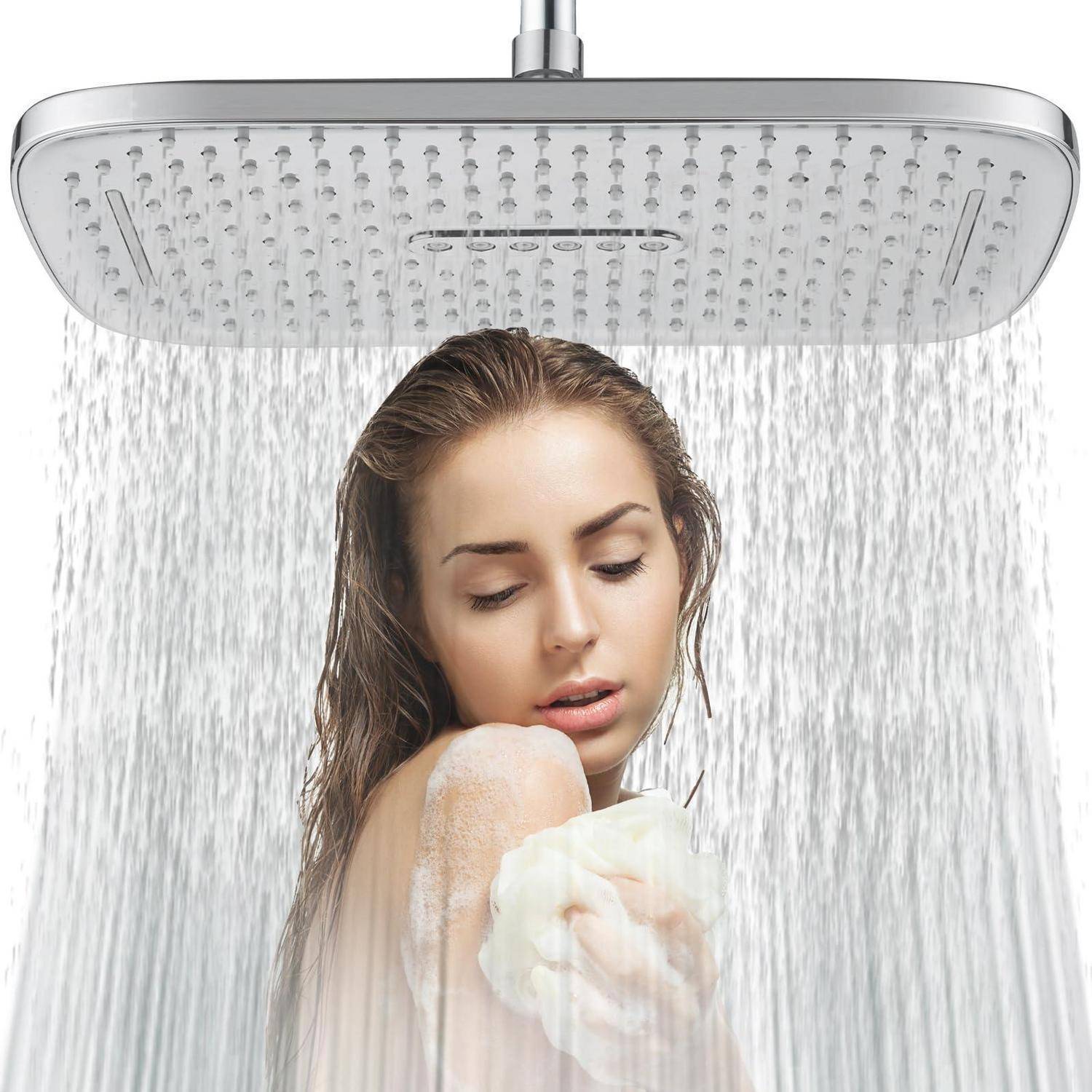 Frau, die unter einem großen Regenduschkopf duscht und ihre Schulter mit einem Schwamm oder Luffa wäscht.