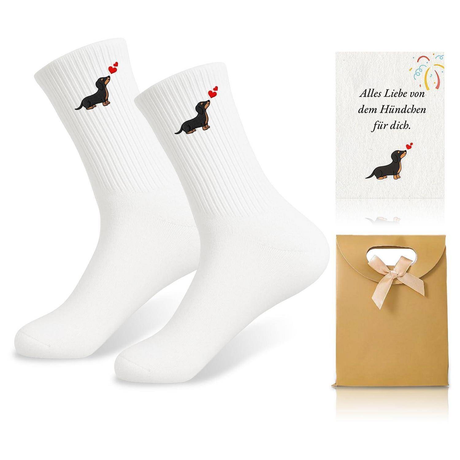 Weiße Socken mit einem kleinen schwarzen Dackel und roten Herzen, gezeigt mit einer deutschen Geschenkkarte mit der Aufschrift „Alles Liebe von dem Hündchen für dich.