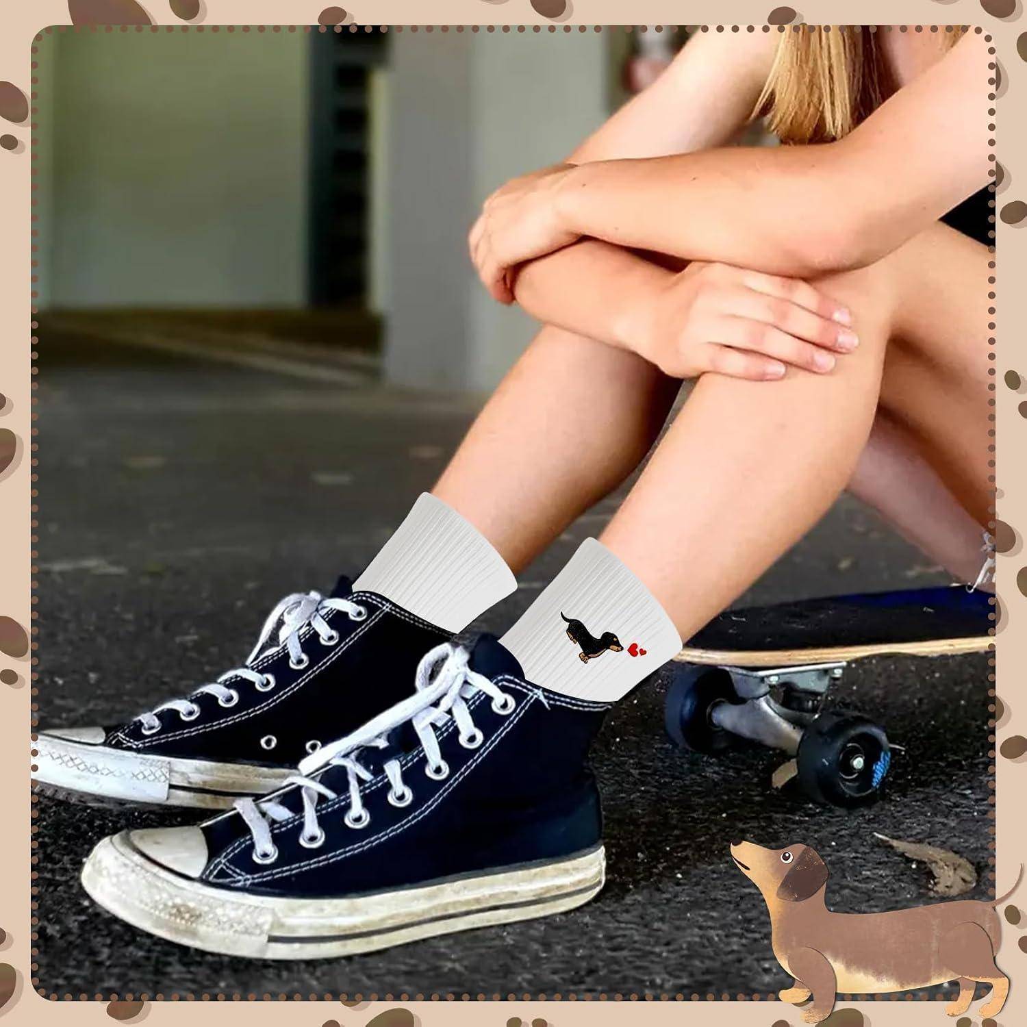 Nahaufnahme einer Person, die mit angezogenen Knien sitzt, schwarze Sneaker und weiße Socken trägt, mit einem kleinen Hundegrafix neben einem Skateboard.