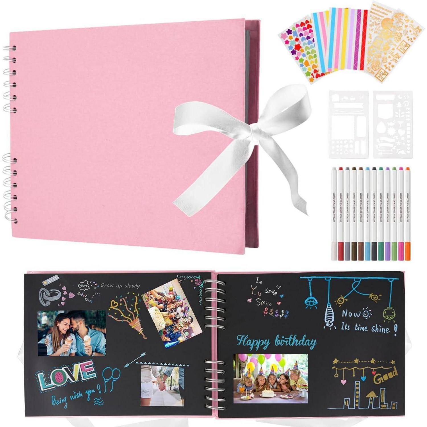 Scrapbook-Set mit einem rosa spiralgebundenem Album, das mit einem weißen Band gebunden ist, Dekorationsstickern, farbigen Stiften und einem Beispiel einer fertigen schwarzen Scrapbook-Seite.