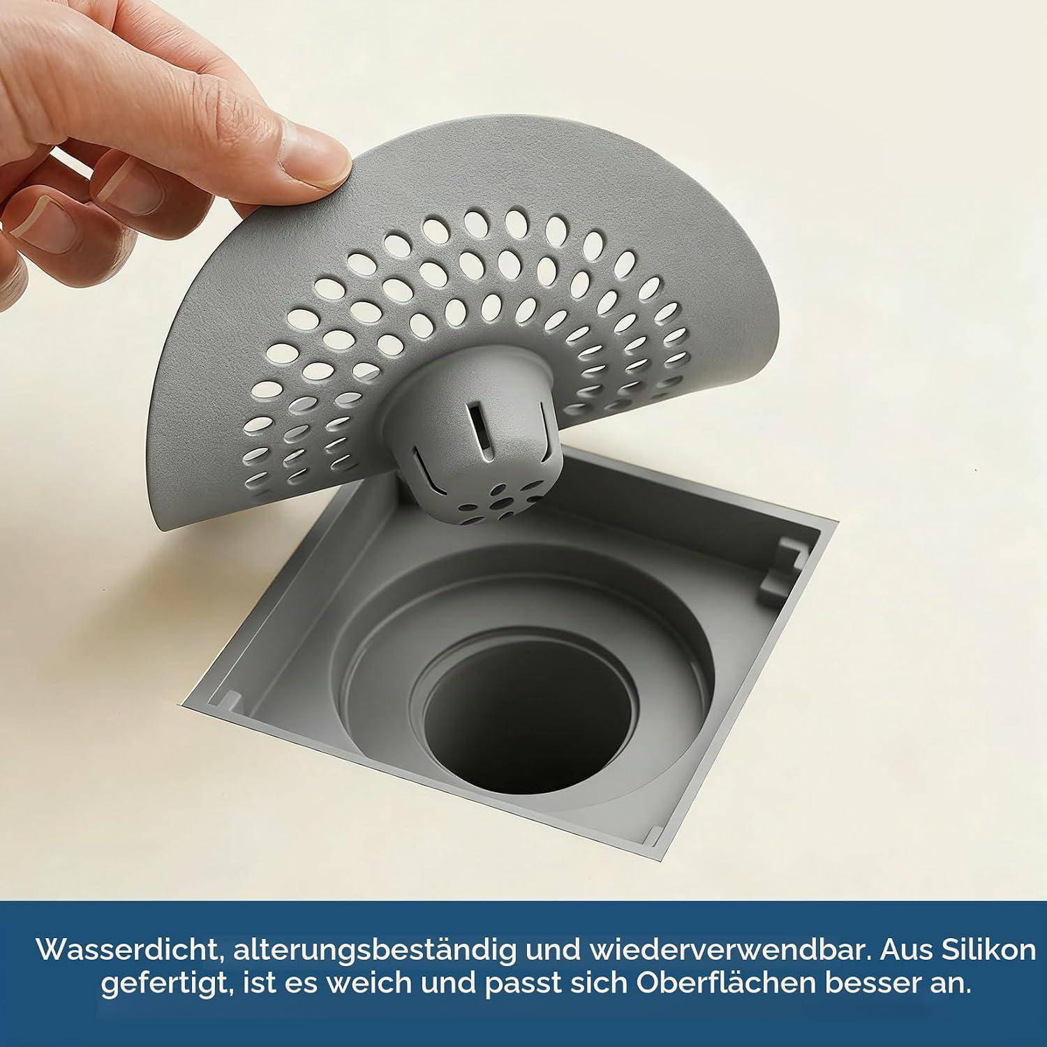 Hand hebt eine flexible graue Silikon-Spülbechenablaufabdeckung mit Perforationen über eine quadratische Ablauföffnung an.