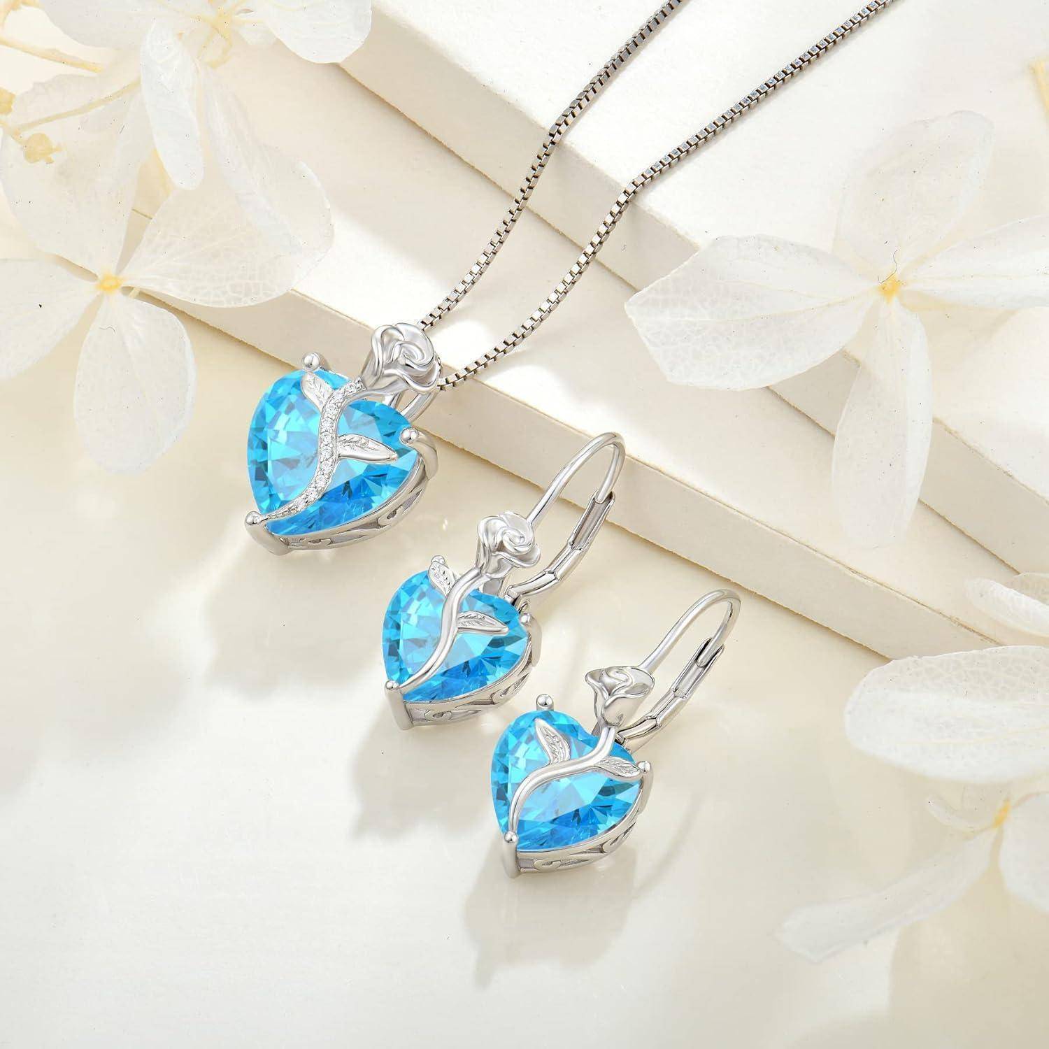Silbernes herzförmiges blaues Edelsteinschmuckset mit Halskette und passenden Ohrrings auf hellflorigem Hintergrund.