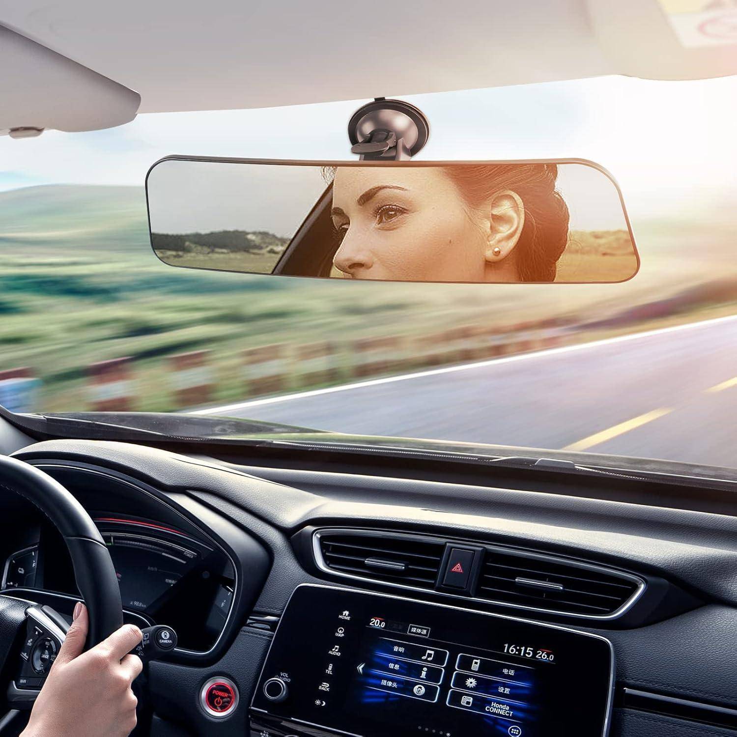 Eine Frau, die an einem sonnigen Tag in einem Auto fährt, gesehen durch den Rückspiegel und die Windschutzscheibe, mit dem sichtbaren Armaturenbrett und Lenkrad.