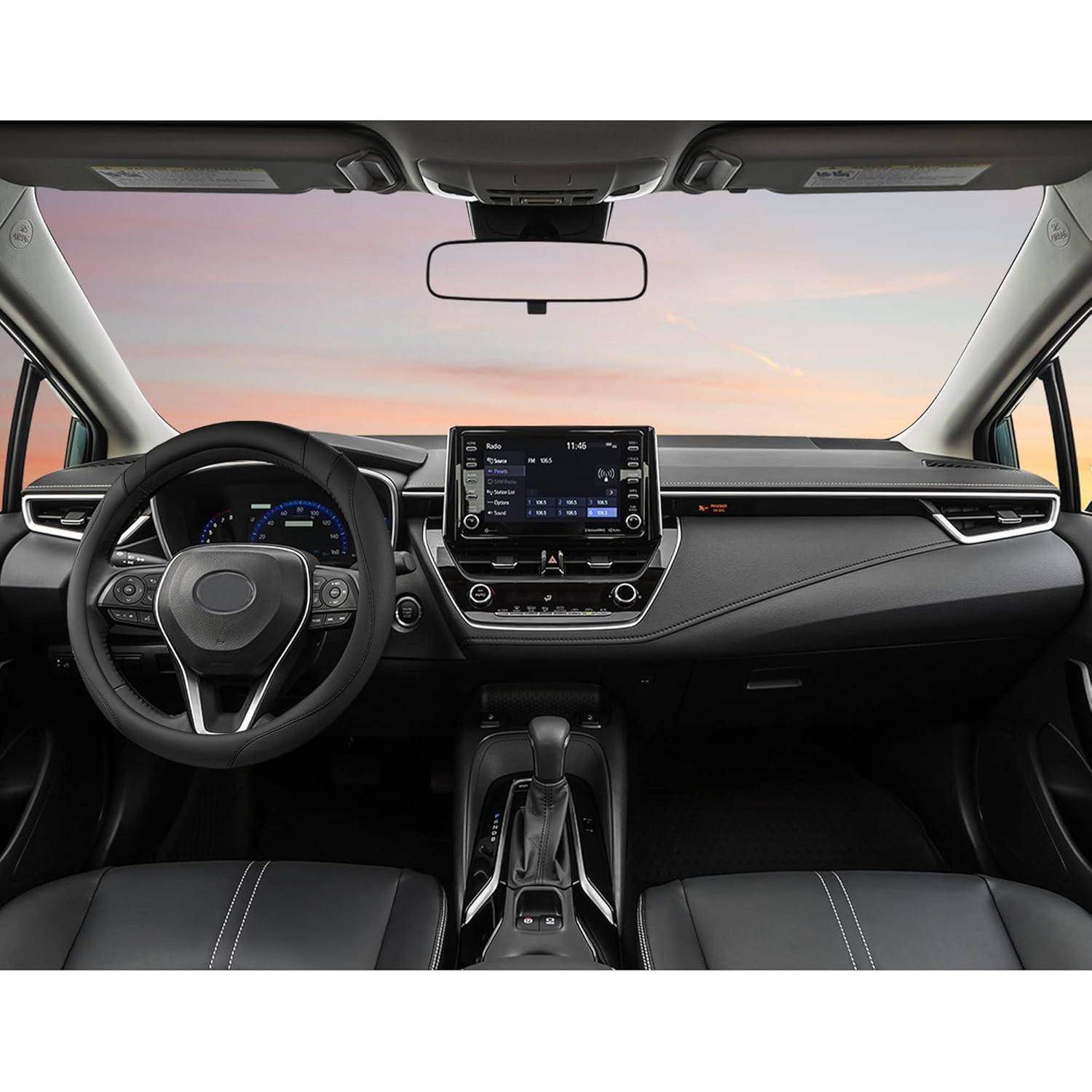 Autoinnenraum aus der hinteren Sitzreihe betrachtet, mit Blick auf das Lenkrad, das digitale Armaturenbrett, den zentralen Touchscreen und den Schaltknüppel vor einem Sonnenuntergangshimmel durch die Windschutzscheibe.