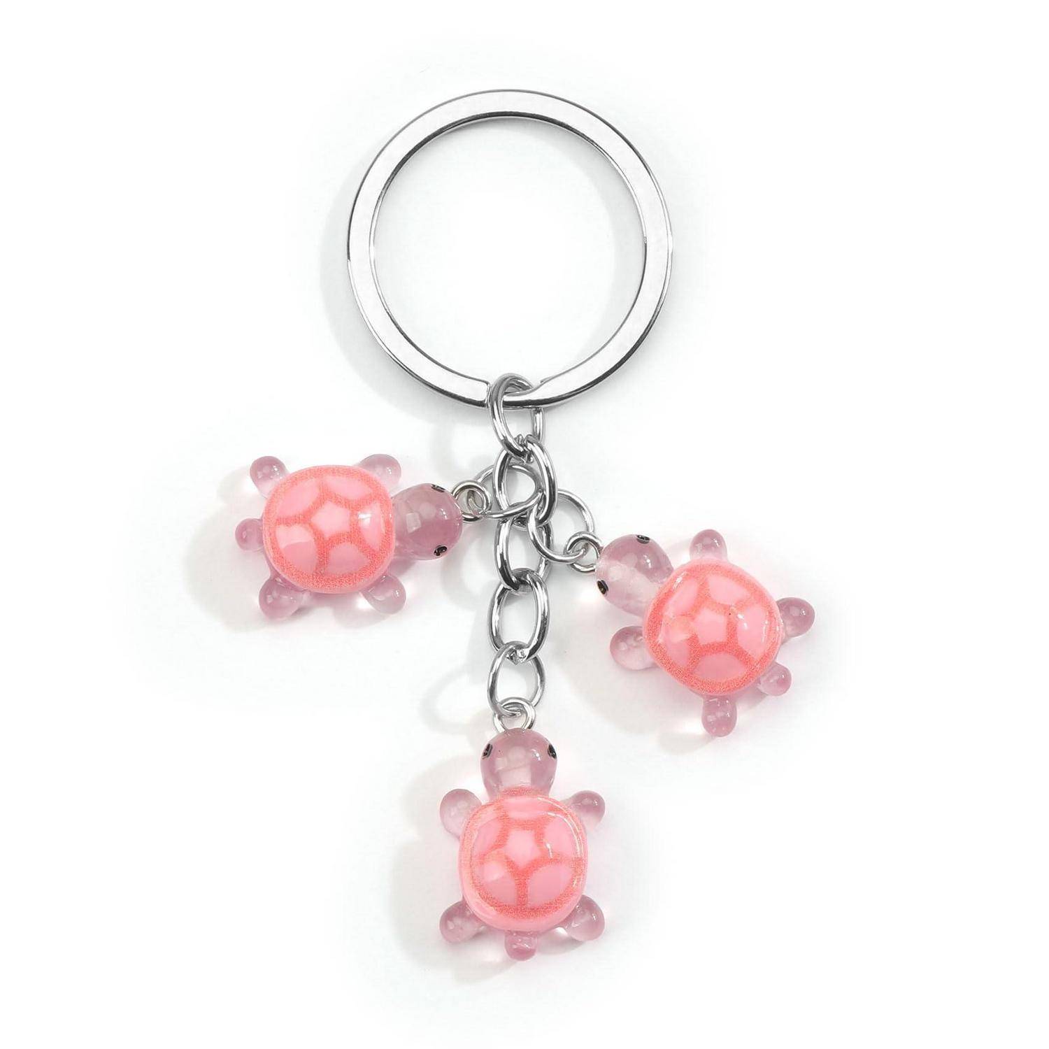 Schlüsselanhänger mit drei rosa Schildkröten-Anhängern, die an einem silbernen Ring an weißem Hintergrund hängen.