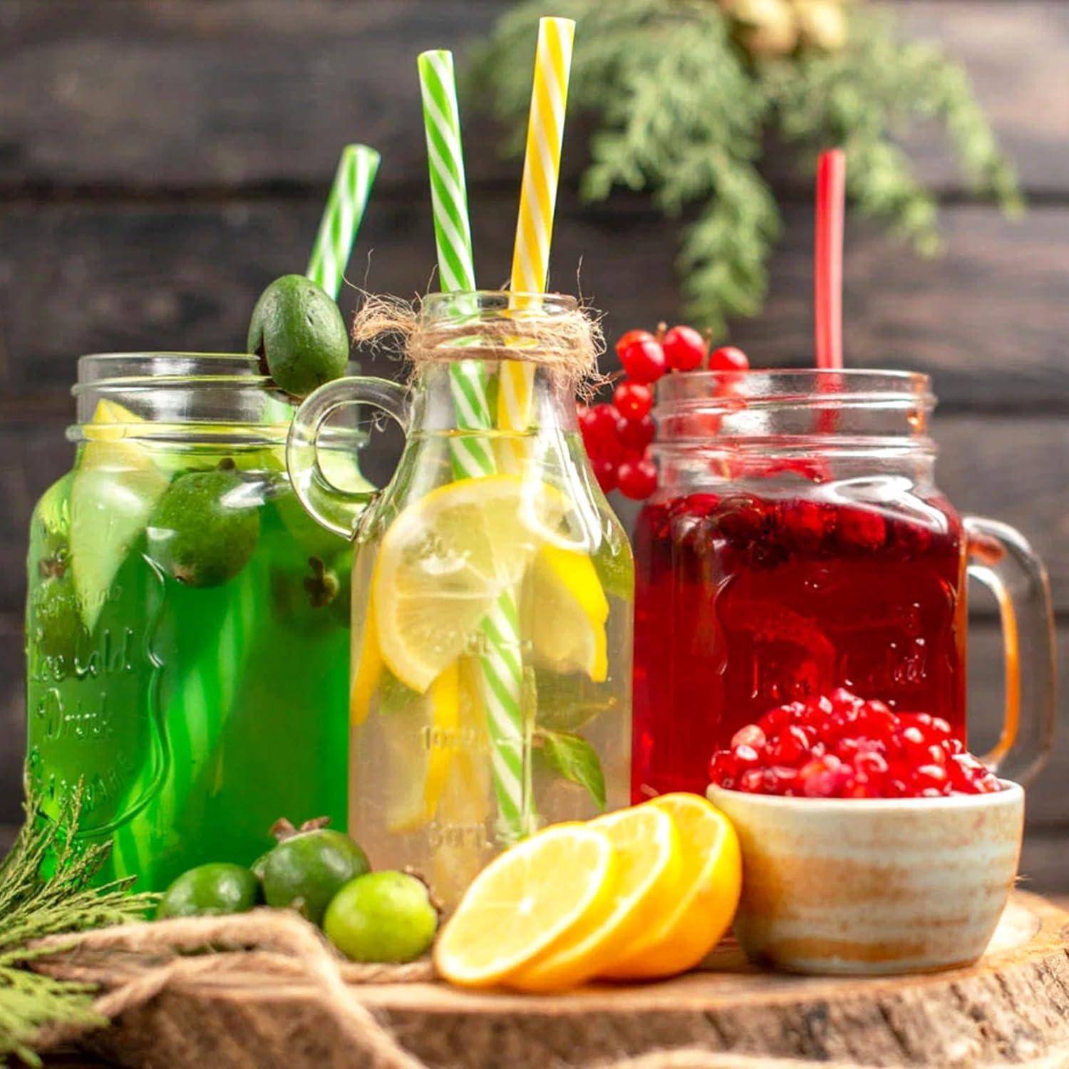 Drei Einmachgläser mit farbenfrohen Fruchtsaftgetränken – grün, Zitrone und rot – serviert mit gestreiften Strohhalmen, Zitrusscheiben und Beeren auf einem Holzbrett.