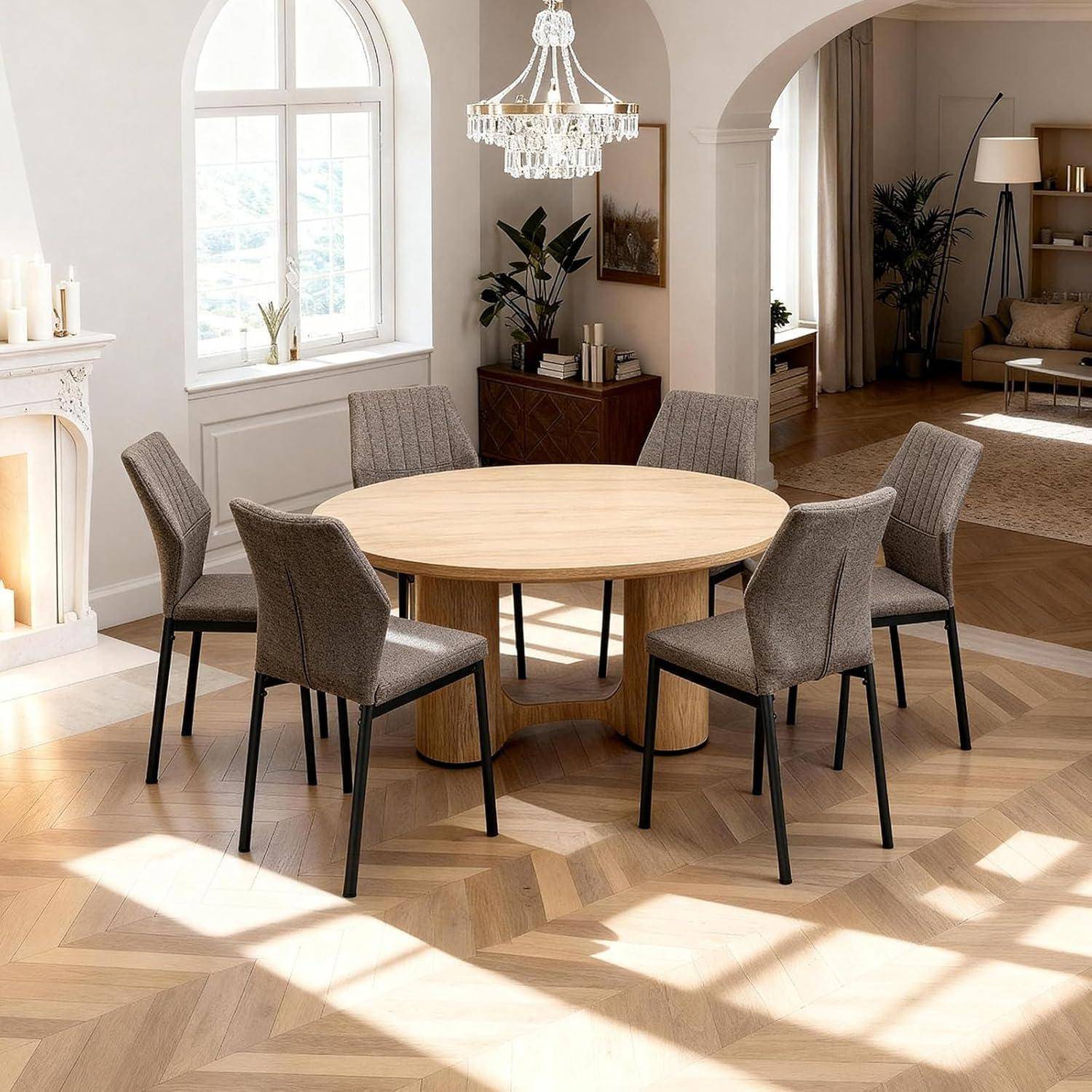 Runder Holzesstisch mit vier gepolsterten grauen Stühlen in einem hellen, modernen Raum mit Bogenfenstern, Kronleuchter und Fischgrätparkett.