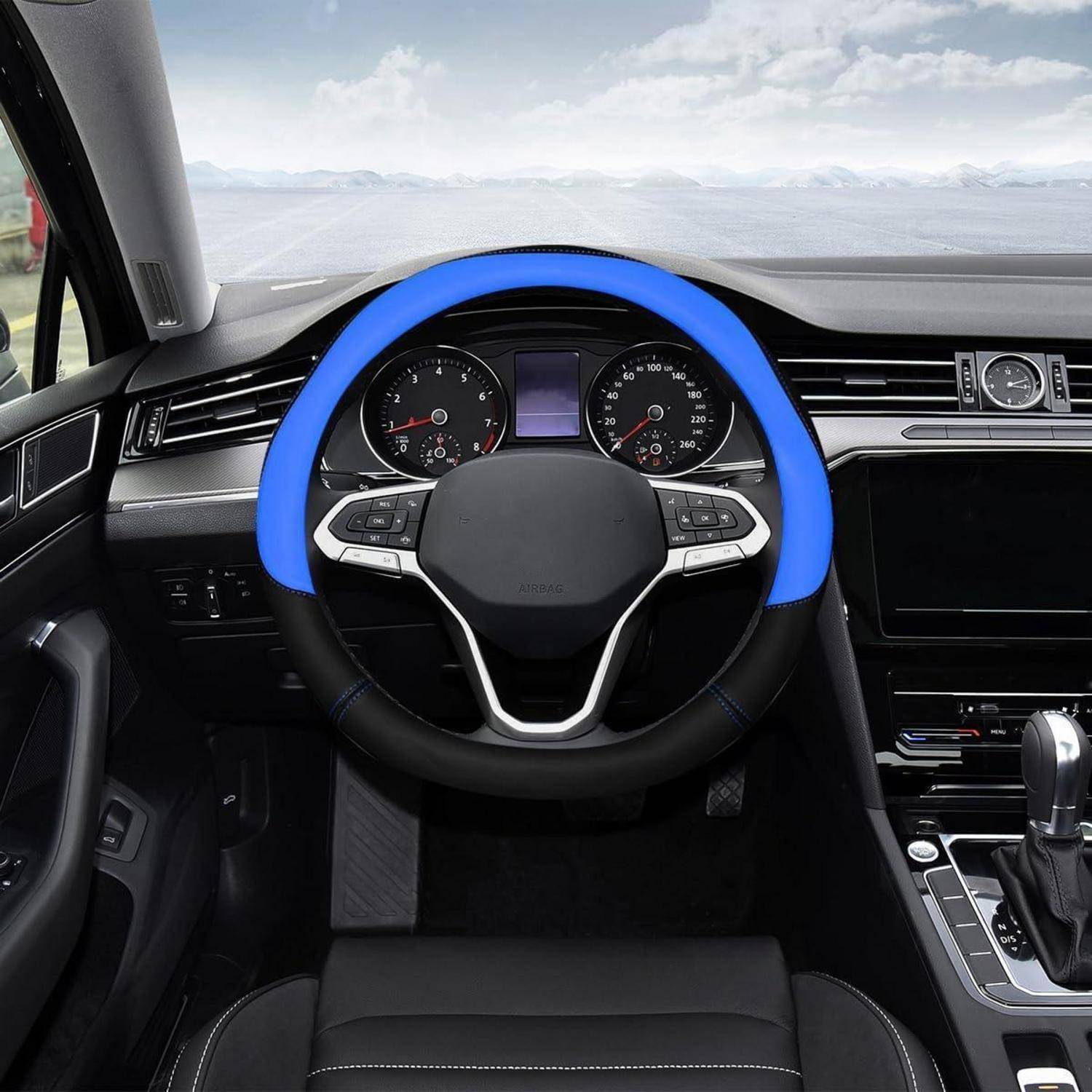 Fahrerplatzansicht eines Autoinnenraums mit einer blauen Lenkradabdeckung, Armaturenbrett-Anzeigen, mittlerer Konsole und einem See, der durch die Windschutzscheibe sichtbar ist.