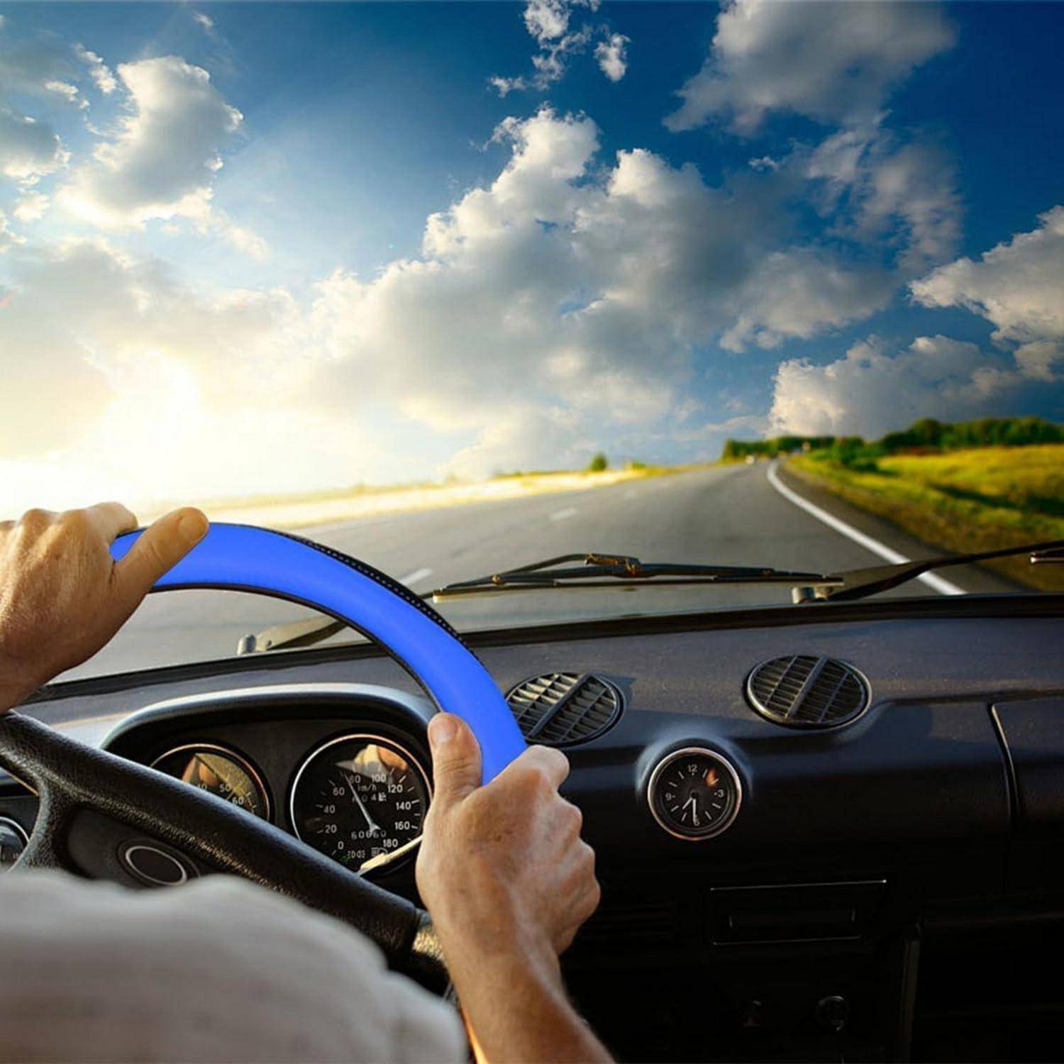 Die Hände eines Fahrers liegen auf einem Lenkrad, während er auf einer offenen Straße unter einem bewölkten Himmel fährt.