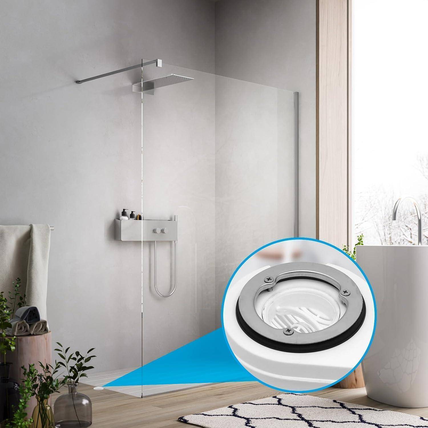 Modernes Badezimmer mit einer Glasduschabtrennung, hervorgehoben durch eine eingefügte Nahaufnahme eines bündig eingelassenen Bodenduschablaufs mit Metallring und Schrauben.