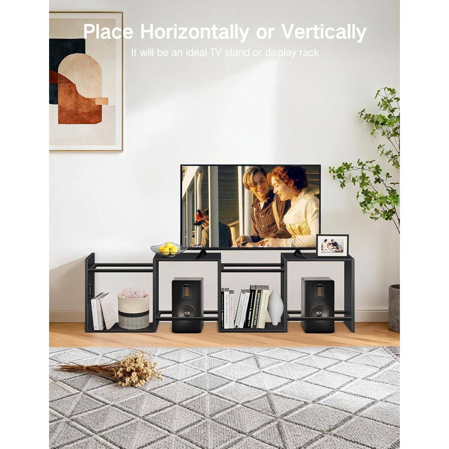 Moderner TV-Ständer mit einem Flachbildfernseher auf einer niedrigen schwarzen Regalbaugruppe, Bücher und Lautsprecher darunter, in einem hellen Wohnzimmer gezeigt; Text besagt „Horizontal oder vertikal platzierbar".