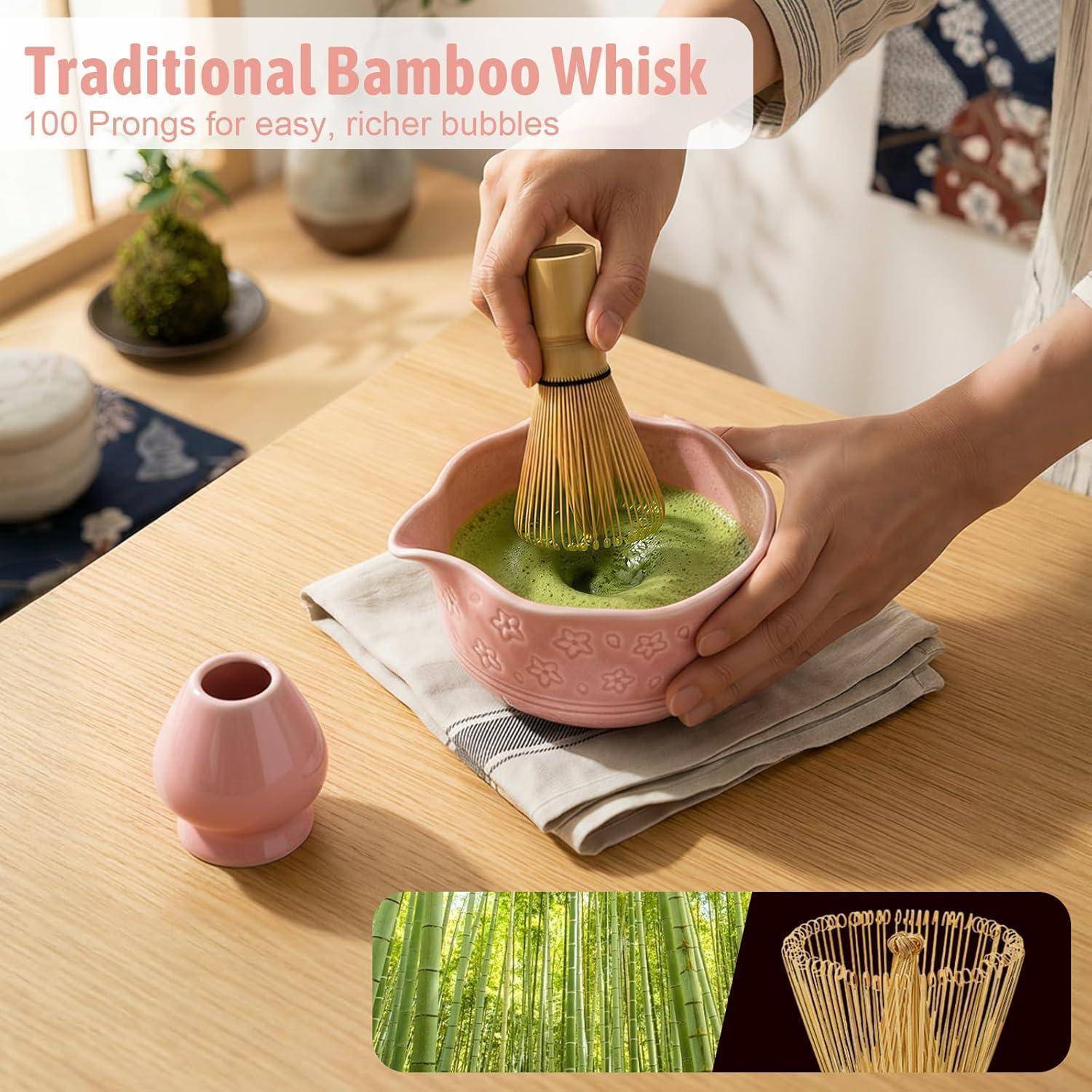Person, die in einer rosa Schale cremigen grünen Matcha mit einem traditionellen Bambusquirl aufschlägt; der Text lautet „Traditioneller Bambusquirl" und „100 Zinken für einfachere, reichhaltigere Blasen"".