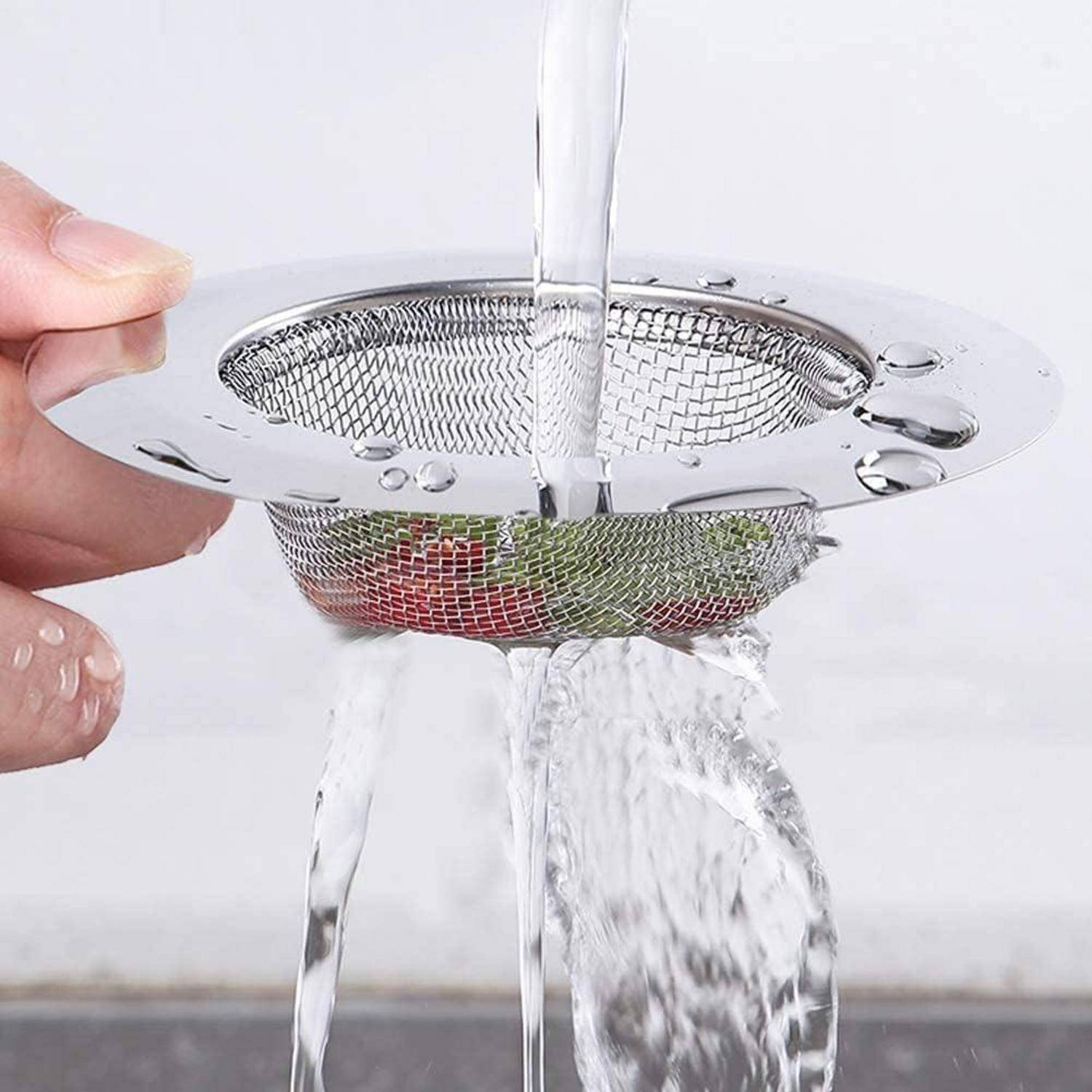 Hand hält einen Edelstahl-Spülensieb unter fließendem Wasser, wobei Wasser durch das Maschengeflecht abfließt, während Essensreste aufgefangen werden.