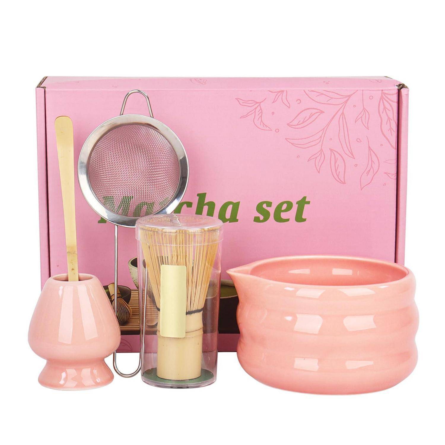 Rosafarbenes Matcha-Tee-Set mit Schachtel, Schüssel, Schneebesen, Sieb, Bambuslöffel und Ständer auf weißem Hintergrund angeordnet.