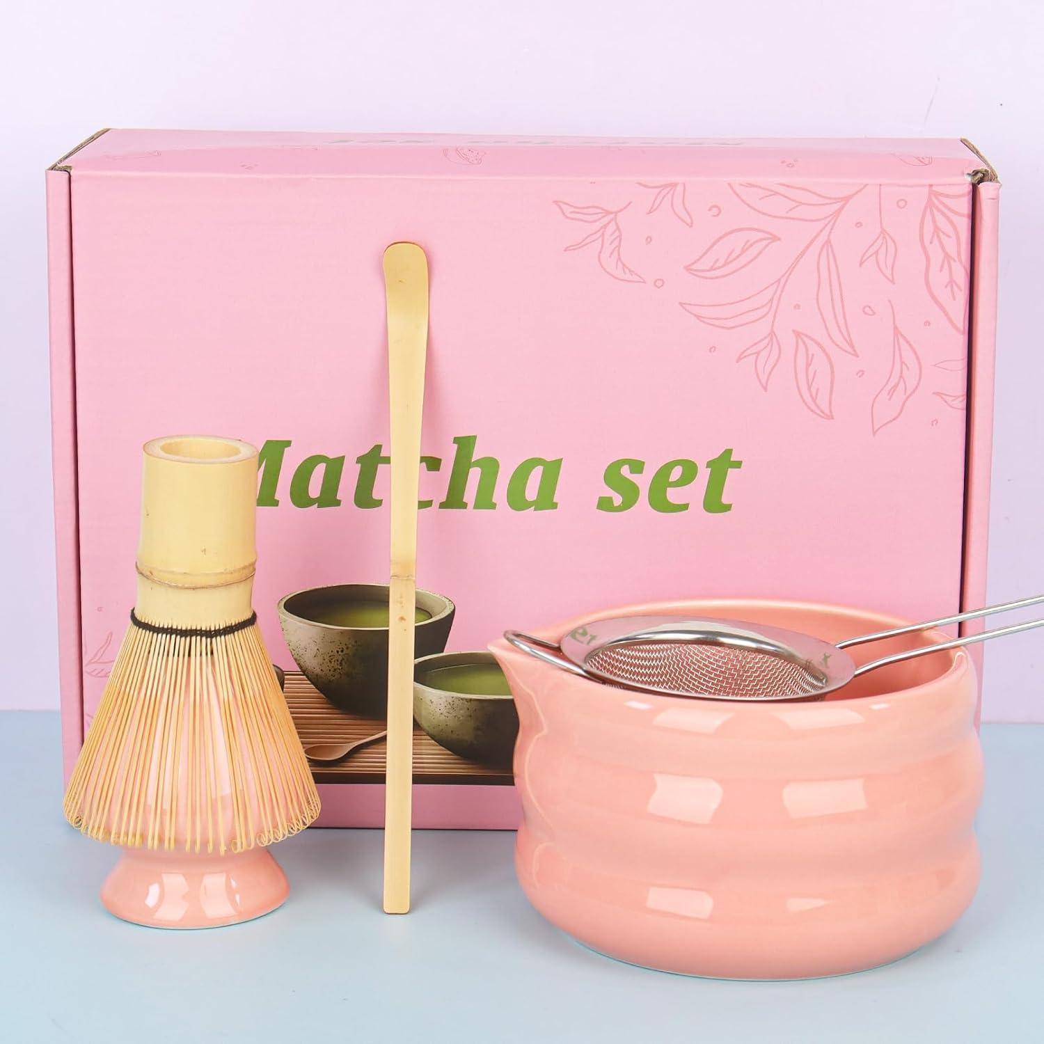 Rosa Matcha-Set mit Bambusquast, Löffel, Schalen, Sieb und verschlossener Rührschale vor einer „Matcha-Set"-Box.