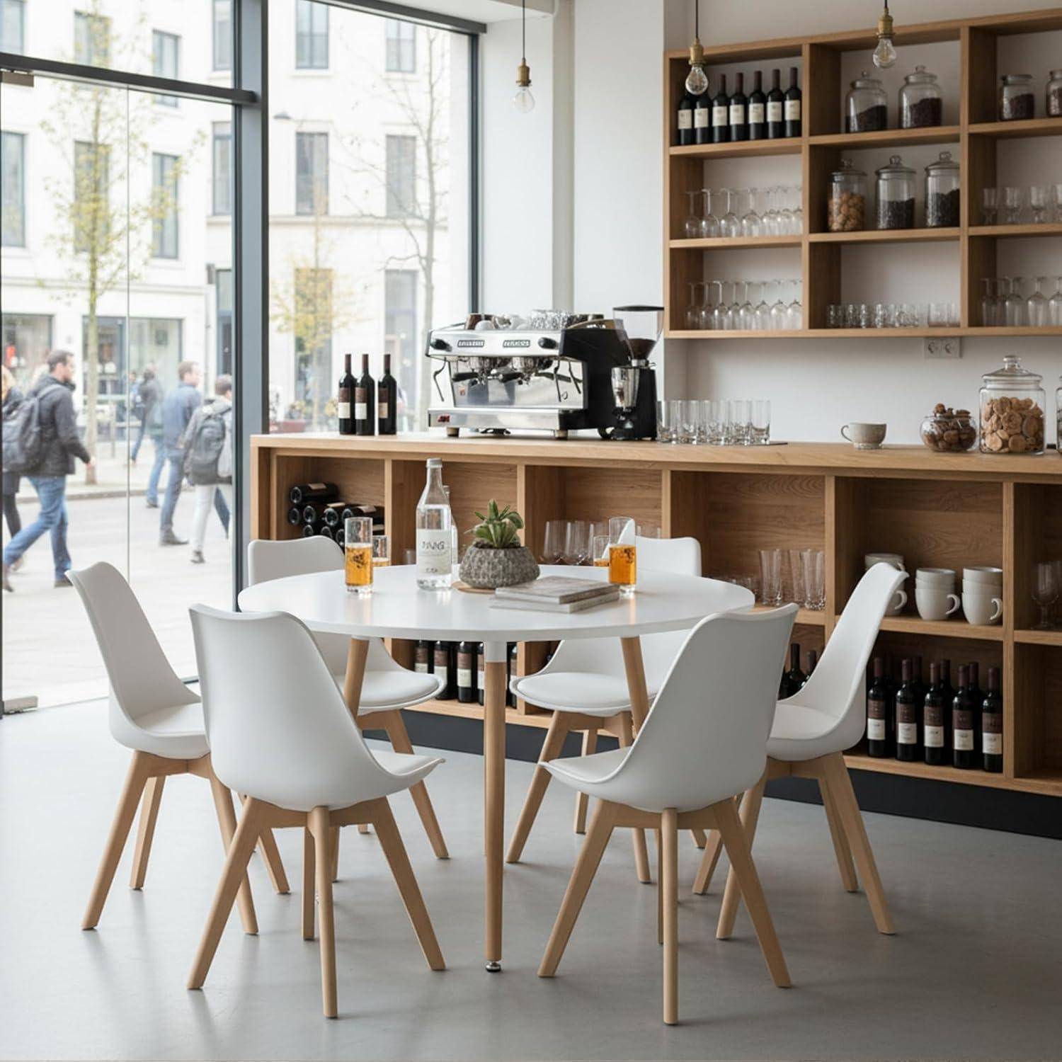 Helles modernes Cafés-Interieur mit weißen runden Tischen und Stühlen, einer Kaffeemaschine auf einem Holztresen und Regalen mit Gläsern und Flaschen an großen Fenstern.
