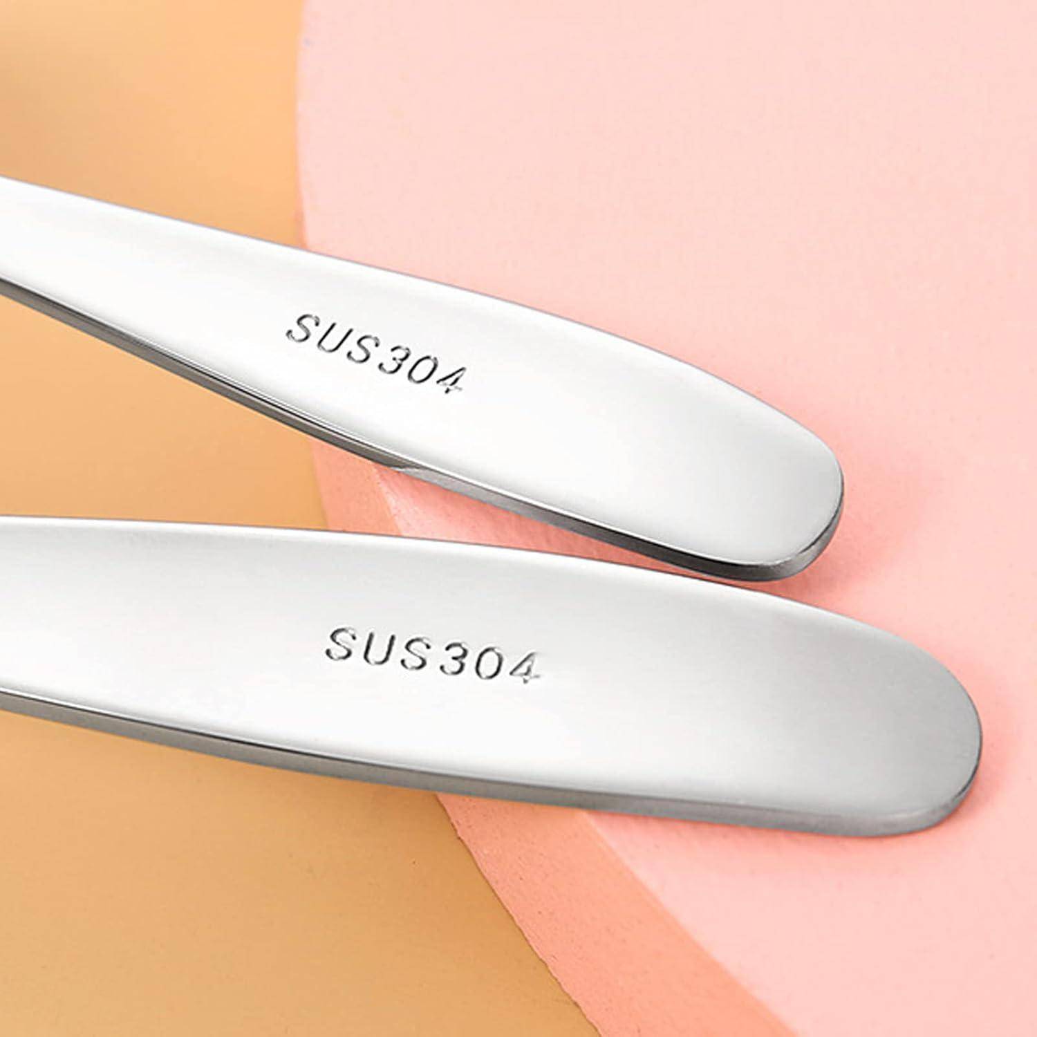 Nahaufnahme von zwei Edelstahlwerkzeugen oder -utensilien mit der Bezeichnung "SUS304"" auf einem rosa und beige Hintergrund.