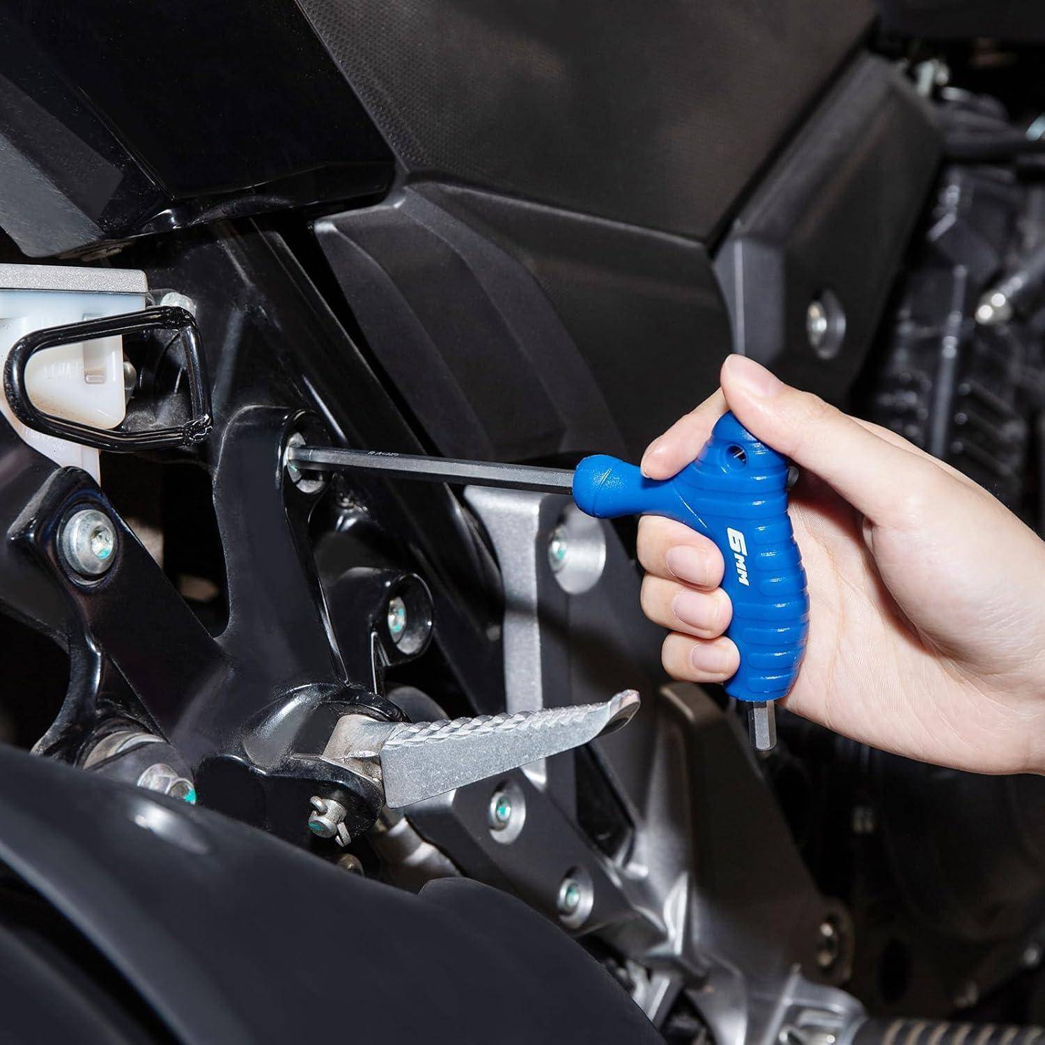 Eine Hand benutzt einen blauen Innensechskantschlüssel, um eine Motorrad-Fußraste oder Rasten-Baugruppe in der Nähe des Motors einzustellen.