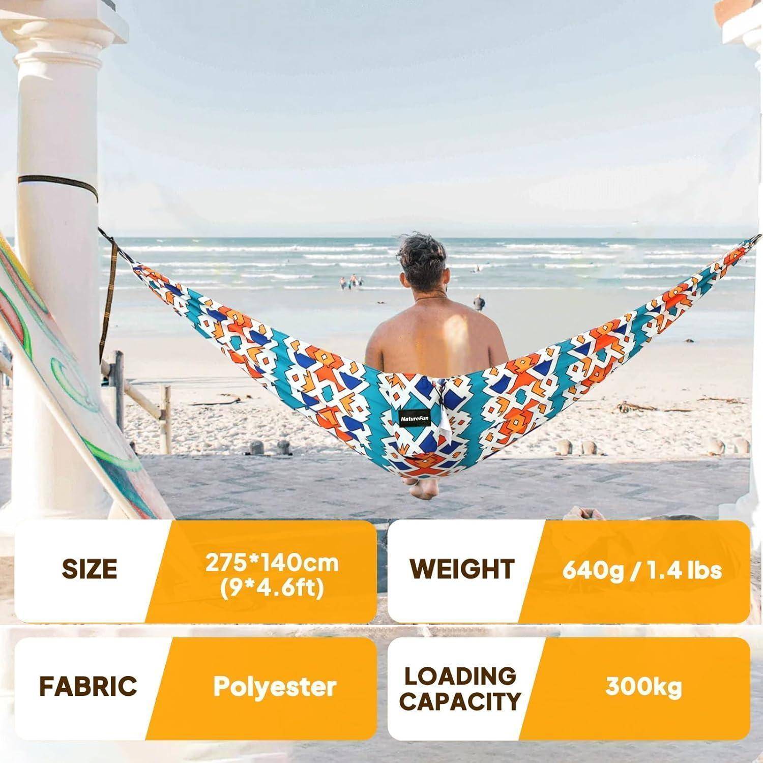 Ein Mann sitzt in einer farbenfrohen hängenden Hängematte mit Blick auf den Strand; Beschriftungen zeigen die Größe 275×140 cm, Stoff Polyester, Gewicht 640 g, Tragfähigkeit 300 kg.