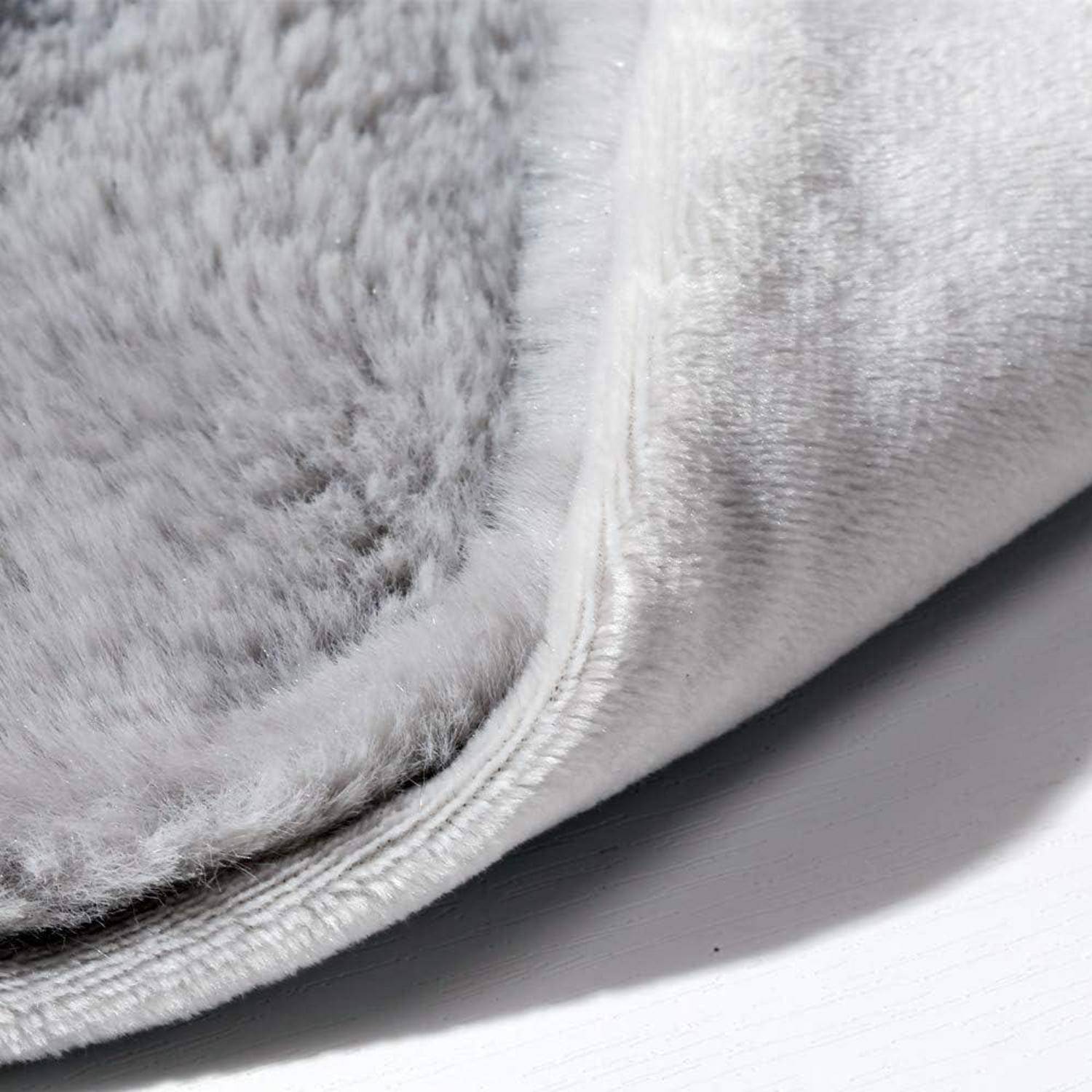 Nahaufnahme einer grauen Plüschstoffkante mit weißem Rippbesatz, die Textur und Nahtdetails auf einer hellen Oberfläche zeigt.