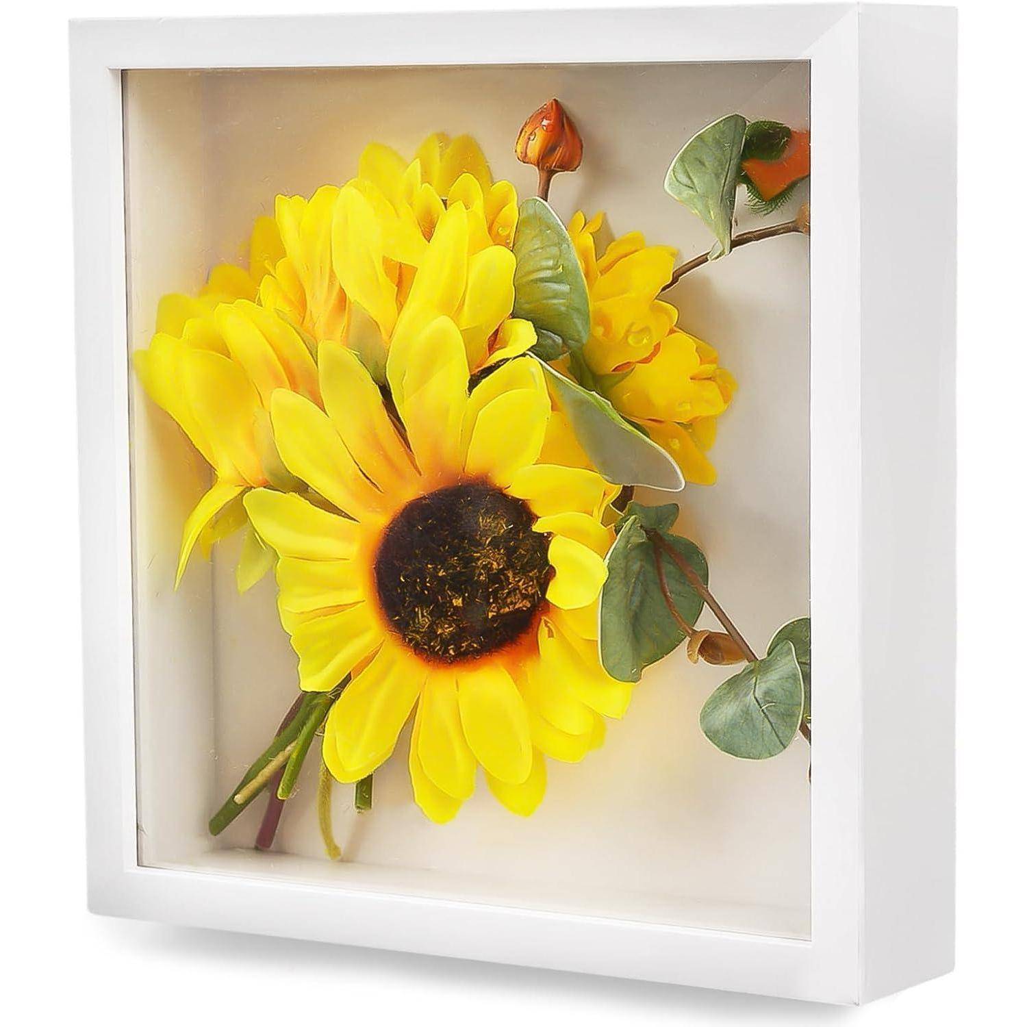 Gerahmte Blumenwandkunst mit leuchtend gelben Sonnenblumen mit grünen Blättern in einem weißen Schattenkastenrahmen.