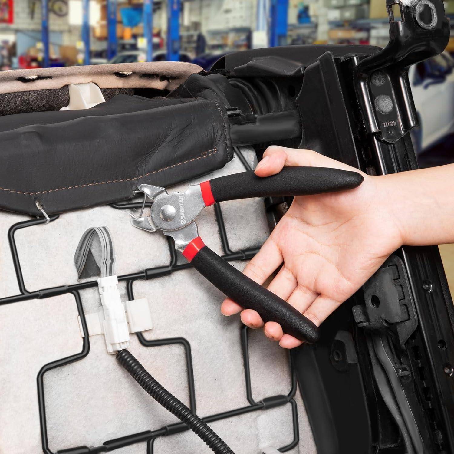 Hand mit Zange zum Schneiden oder Anpassen von Kabeln unter einem Autositz, wobei der Sitzrahmen in einer Werkstatt freigelegt ist.