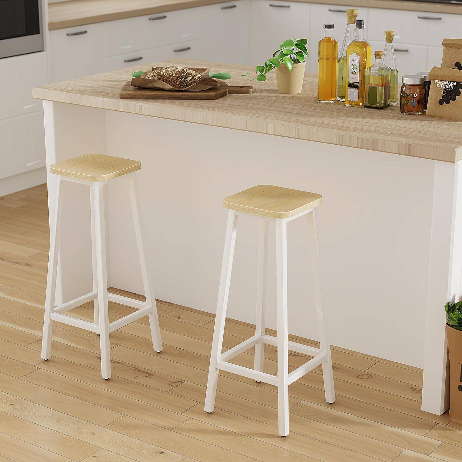 Zwei weiße Barhocker mit hellem Holzsitz stehen an einer Kücheninsel in einer hellen, modernen Küche.