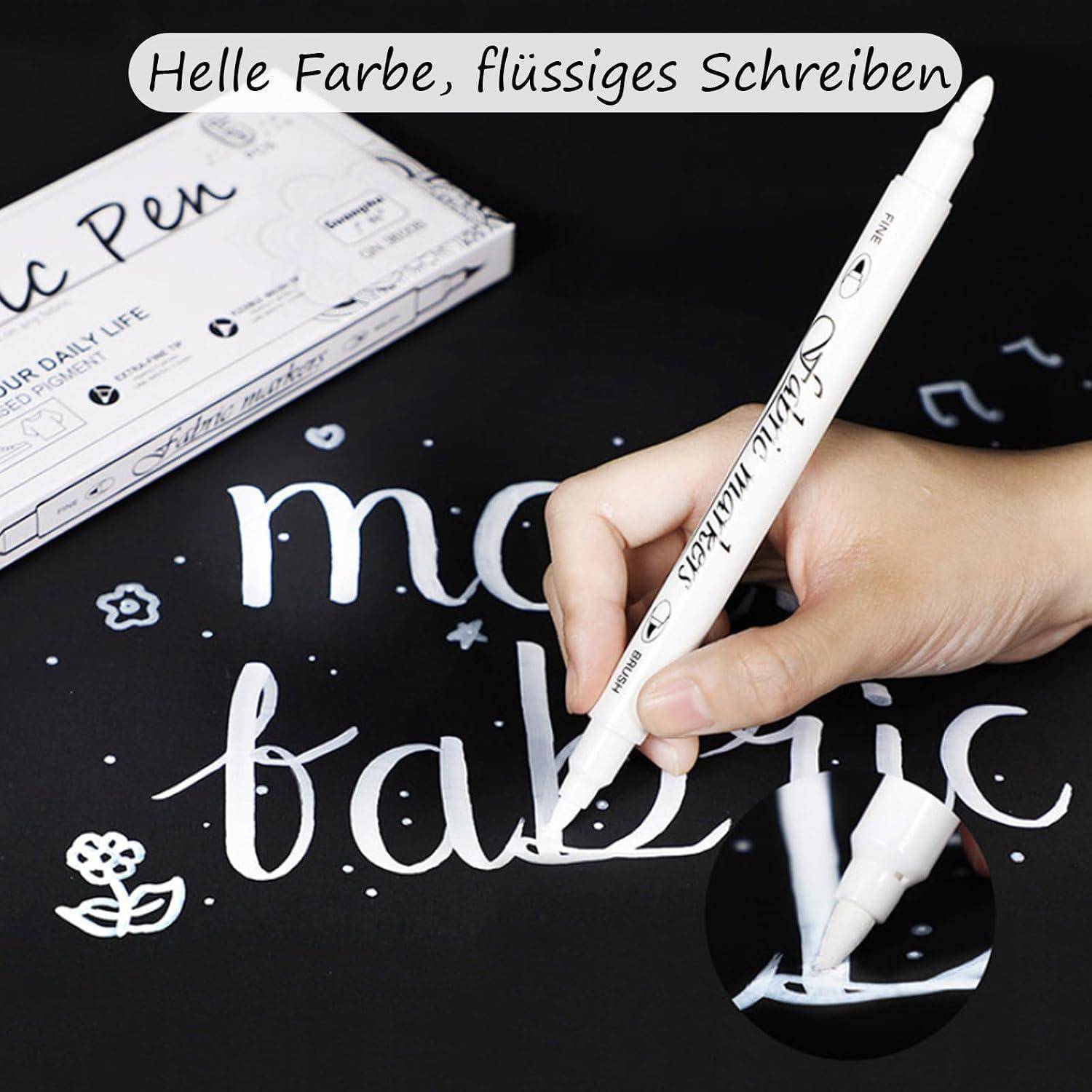 Handschrift mit einem weißen Lackstift auf schwarzem Papier; deutscher Text sagt „Helle Farbe, flüssiges Schreiben" und „mofabrie"" wird gerade geschrieben.
