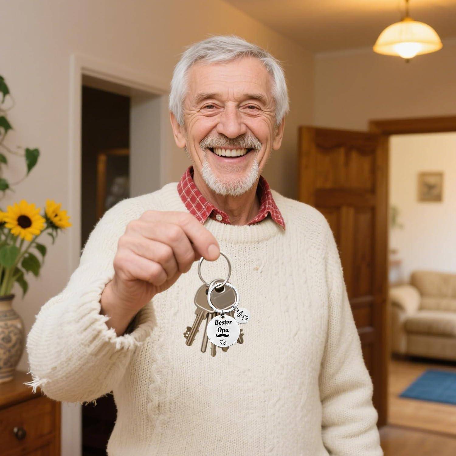 Ein lächelnder älterer Mann in einem Pullover hält einen Schlüsselring mit einem "Bester Opa"" Anhänger in einem gemütlichen Wohnungsinterieur.