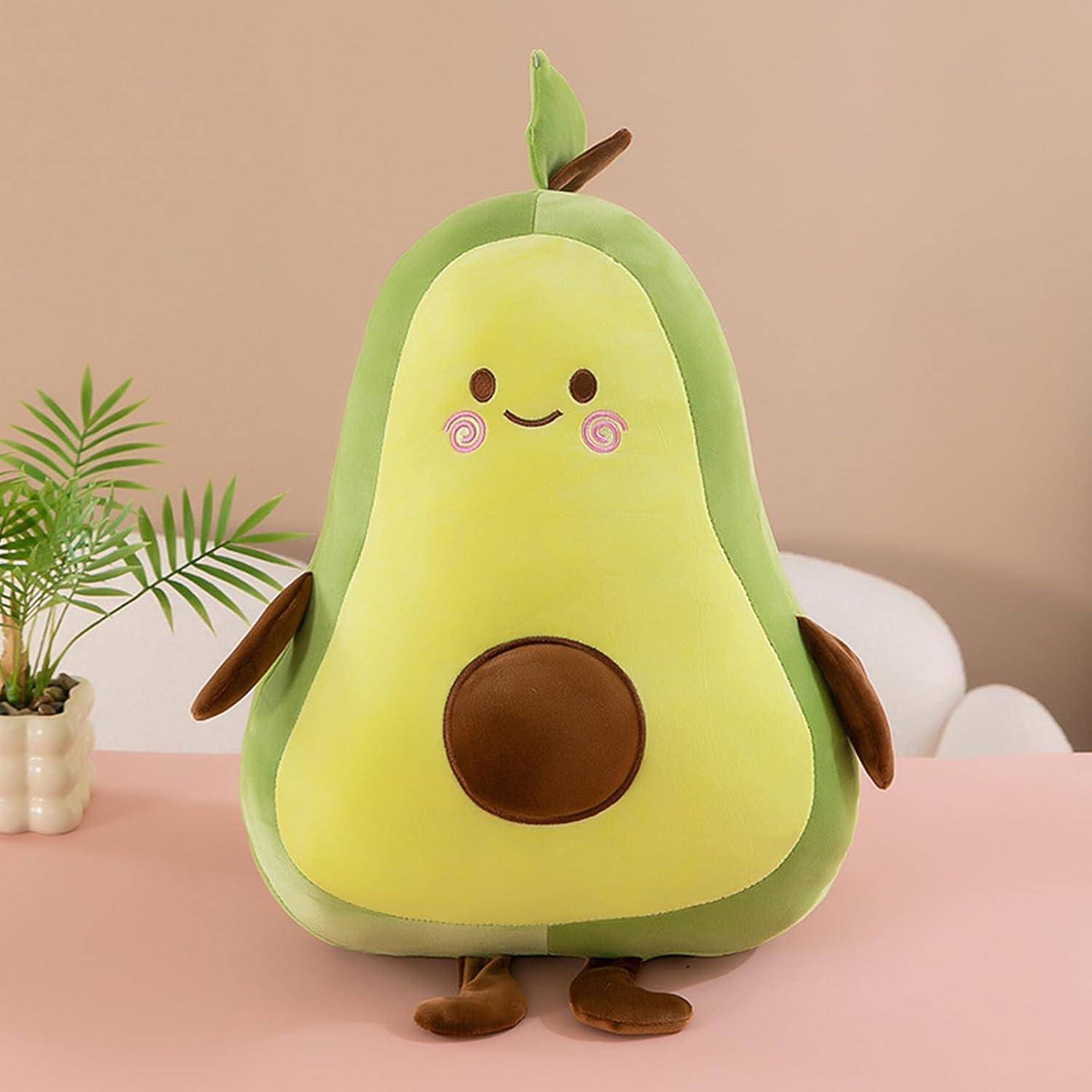 Süsses plüschiges Avocado-förmiges Spielzeug mit einem lächelndem Gesicht, braunem Kern-Bauch und kleinem Blatt, das auf einer rosa Tischplatte sitzt.
