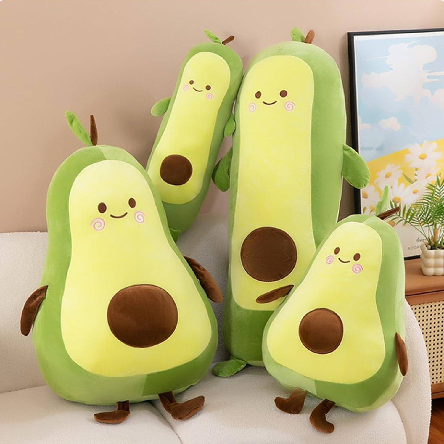 Vier lächelnde Avocado-Plüschtiere in verschiedenen Größen auf einem Sofa angeordnet, mit einem Bild im Rahmen und einer kleinen Pflanze im Hintergrund.