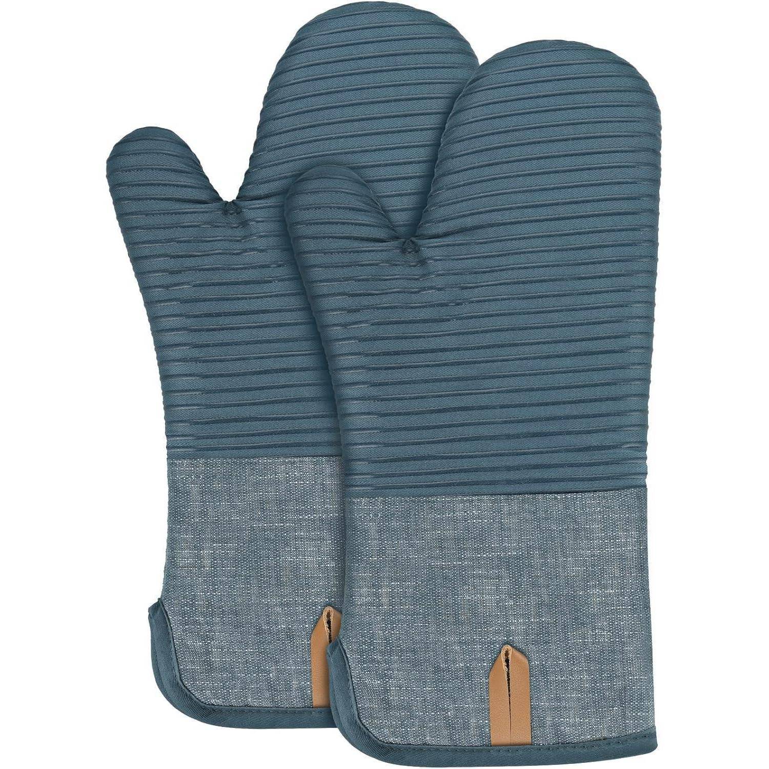 Paar blauer gesteppter Ofenhandschuhe mit jeansähnlichen unteren Manschetten und beigen Aufhängeschleifen auf weißem Hintergrund.