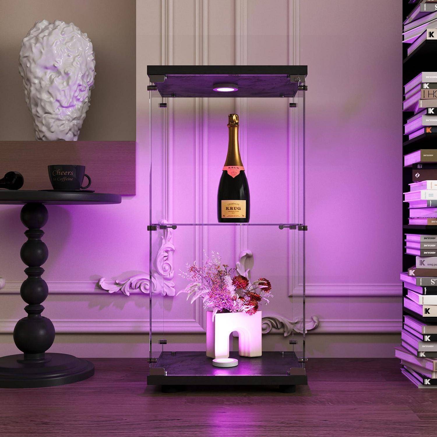 Ein beleuchteter Glasvitrinenschrank enthält eine Champagnerflasche und ein Blumengesteck, mit einem schwarzen Beistelltisch und einer dekorativen Büste in einem violett beleuchteten Raum.