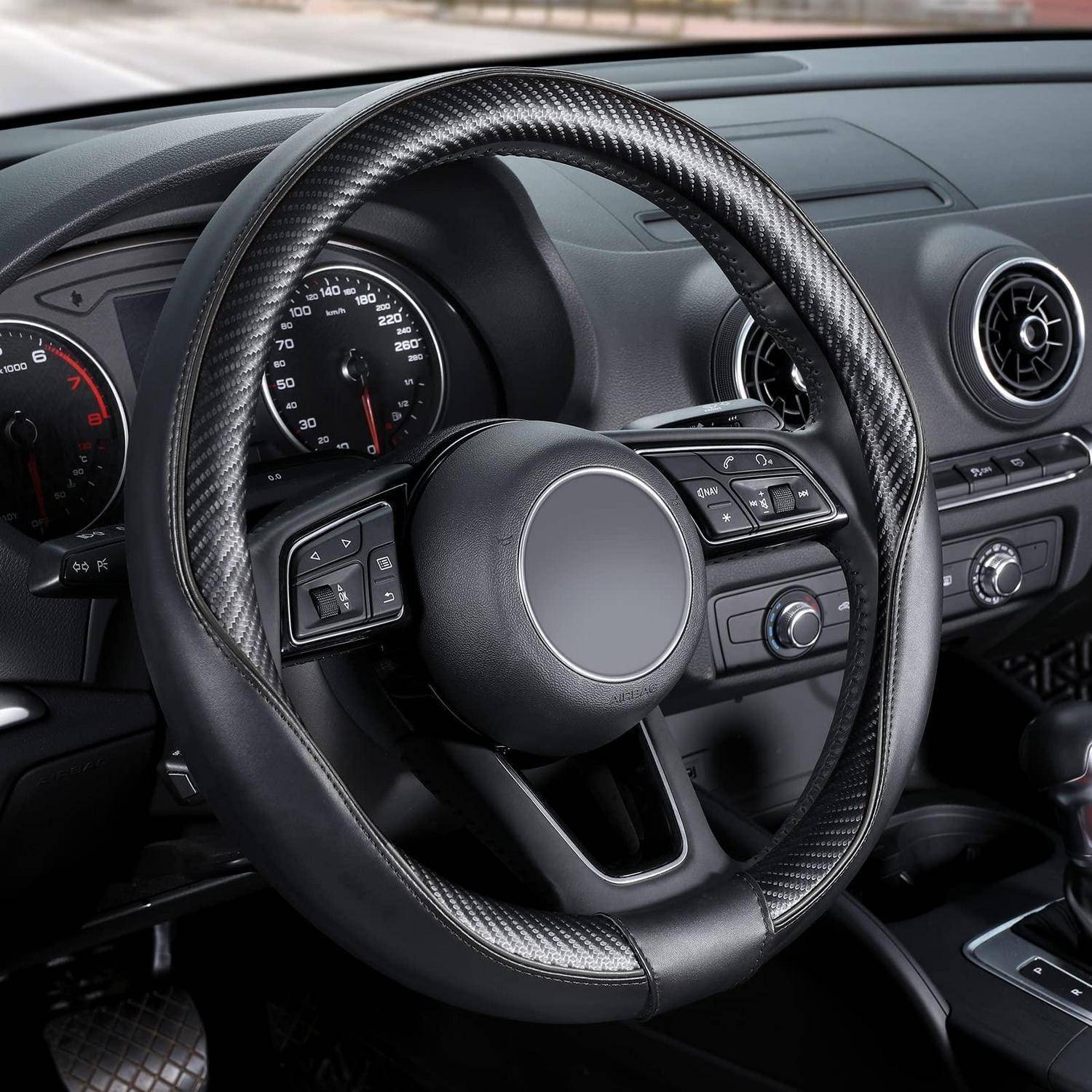 Autoinnere mit einer Nahaufnahme eines schwarzen Lenkrads mit Karbonfaser-Verkleidung, Instrumententafel-Anzeigen, Lüftungsöffnungen und Mittelbedienungen.