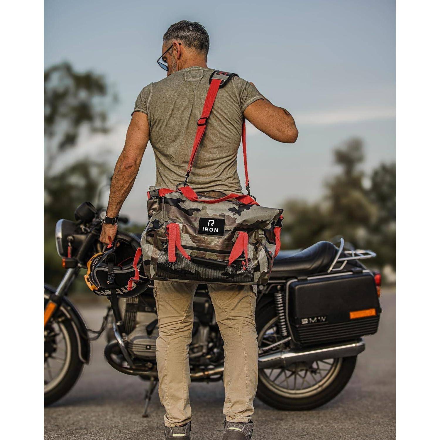 Rückansicht eines Mannes, der neben einem Motorrad steht, in Freizeitkleidung gekleidet und eine rote Umhängetasche trägt, während er einen Helm in der Hand hält.