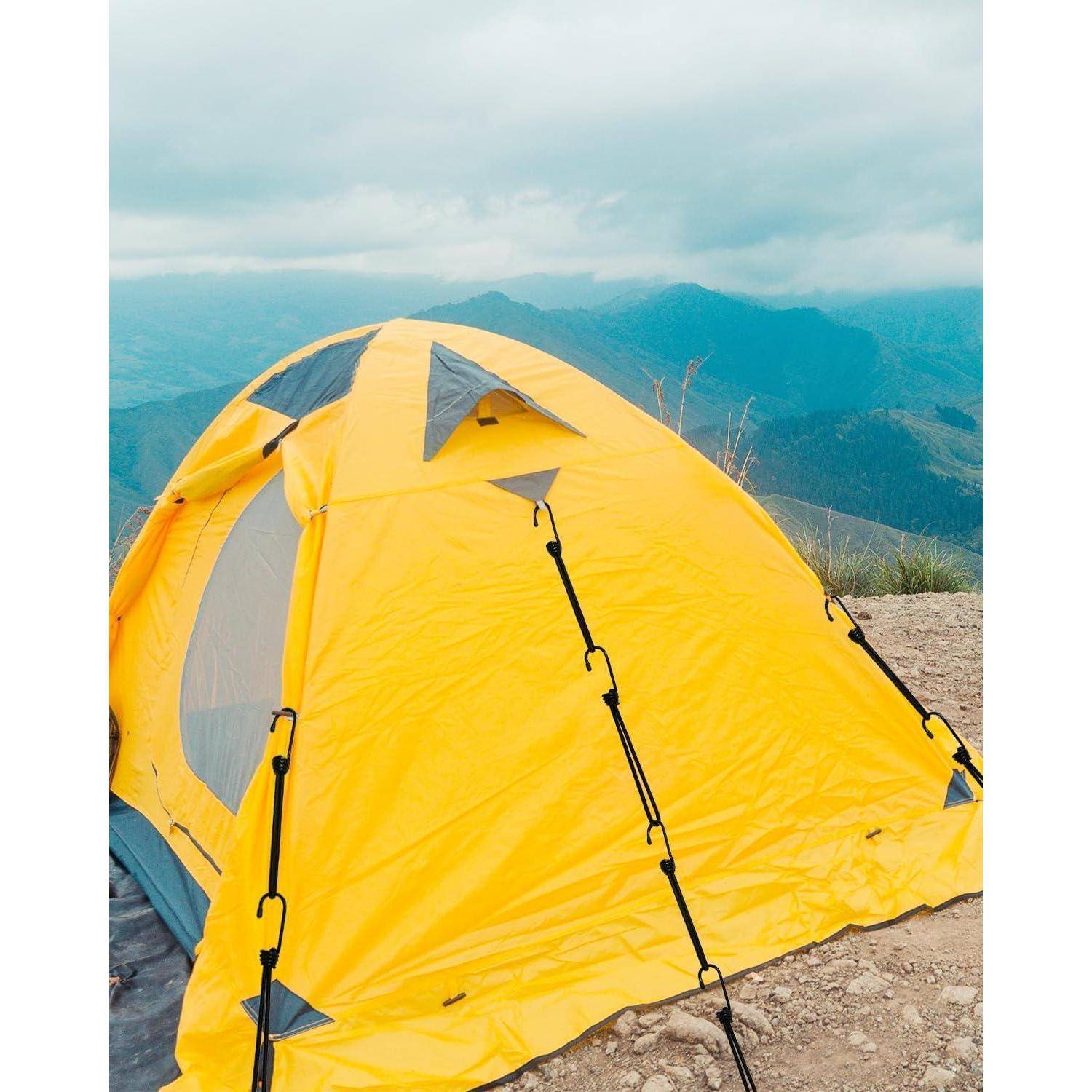 Gelbes Campingzelt auf einem felsigen Berggipfel mit bewölkten blauen Hügeln im Hintergrund aufgestellt.