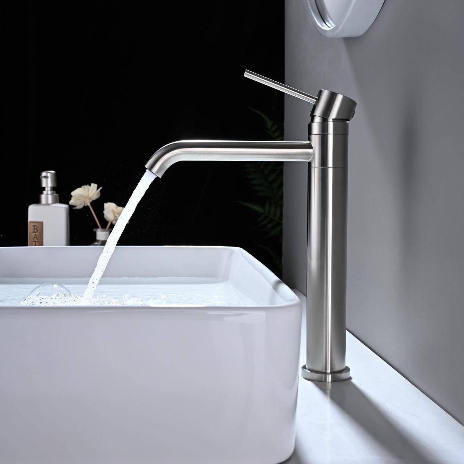 Moderner Edelstahlhahn mit fließendem Wasser in ein weißes Waschbeckken auf einer Arbeitsplatte in einer minimalistischen Badezimmerumgebung.