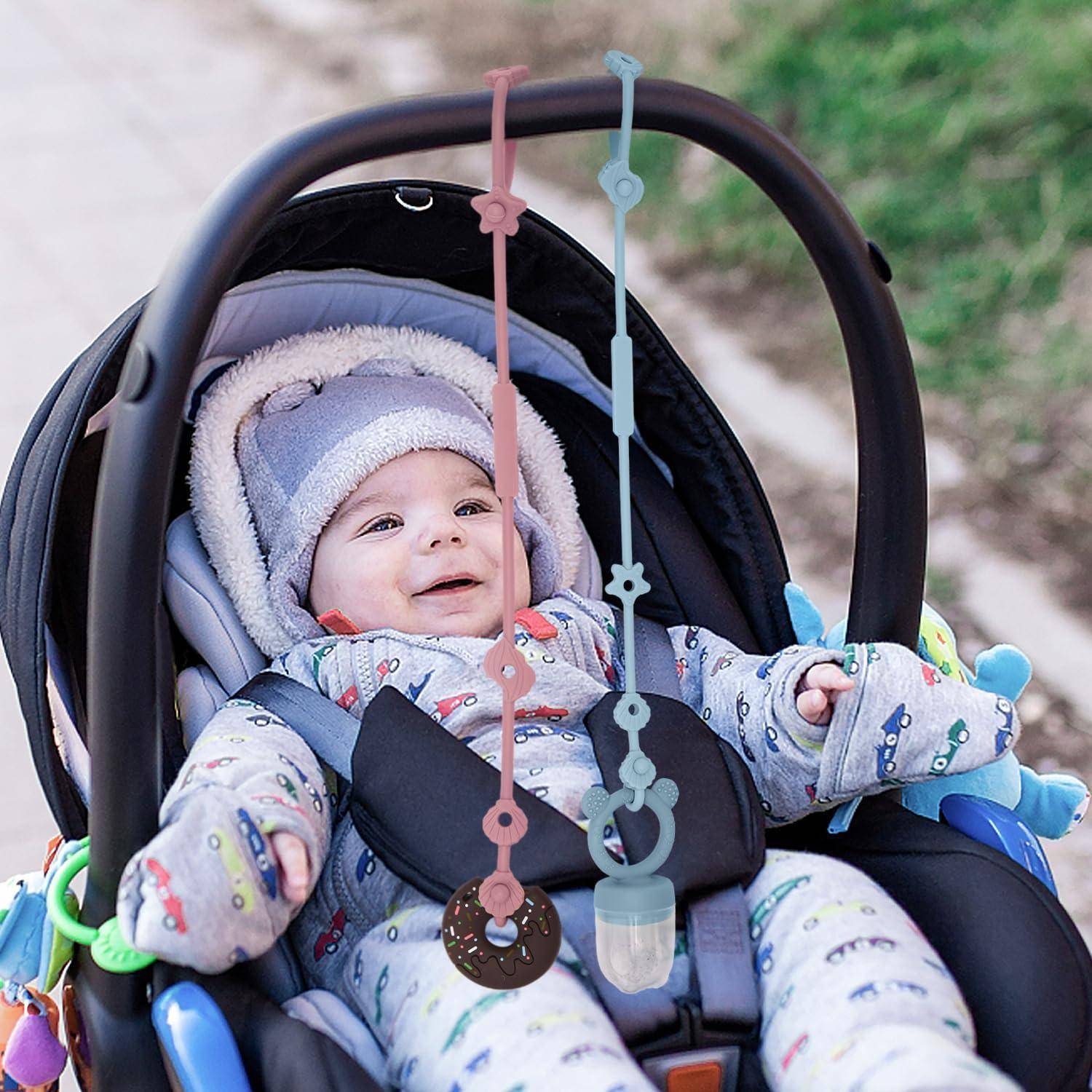 Baby in einem Autositz, das lächelt im Freien, trägt einen Kapuzenwintermantel und ist angeschnallt mit hängenden Spielzeugketten darüber.