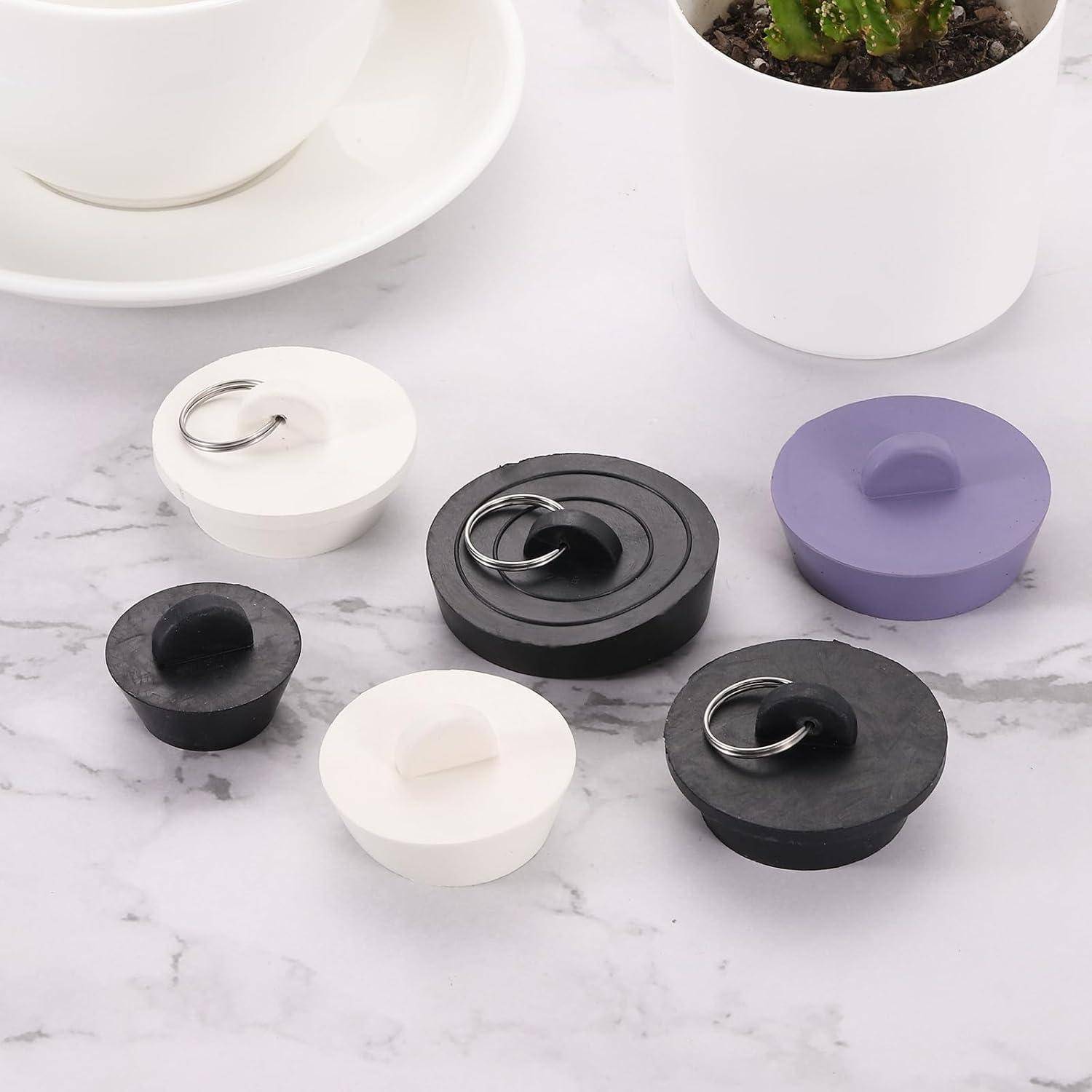 Fünf runde Silikon-Topfdeckelheber mit Ringgriffe in Schwarz, Weiß und Lila auf einer Marmoroberfläche in der Nähe eines Blumentopfs und einer Tasse