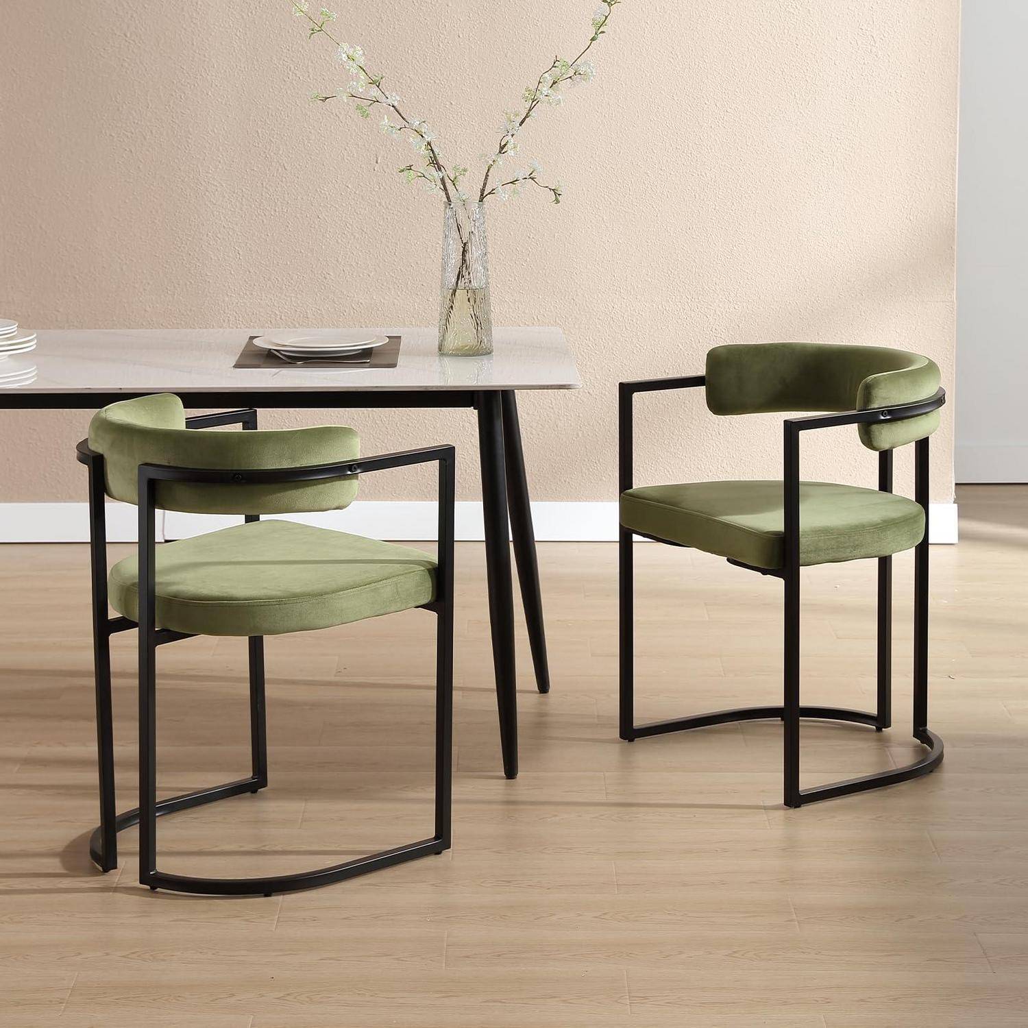 Zwei olivgrün gepolsterte Stühle mit schwarzen Metallrahmen neben einem Tisch aus hellem Holz in einem minimalistischen Esszimmer.