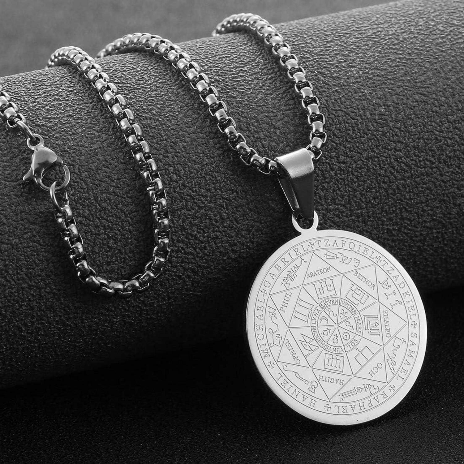 Silberne Anhängerkette mit einer gravierten runden Medaille, ausgestellt auf einem dunkel strukturierten Ständer.