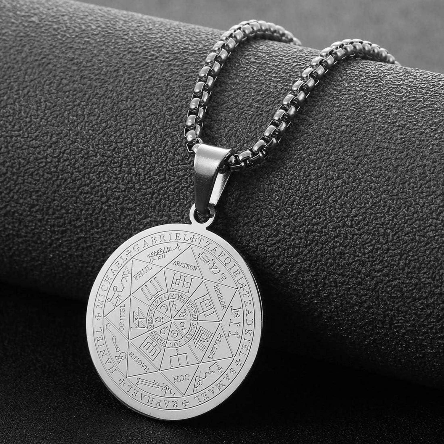 Silberne Anhängerkette mit einem gravierten Kreissymbol-Design an einer schwarzen Kette, fotografiert vor einem dunklen strukturierten Hintergrund.