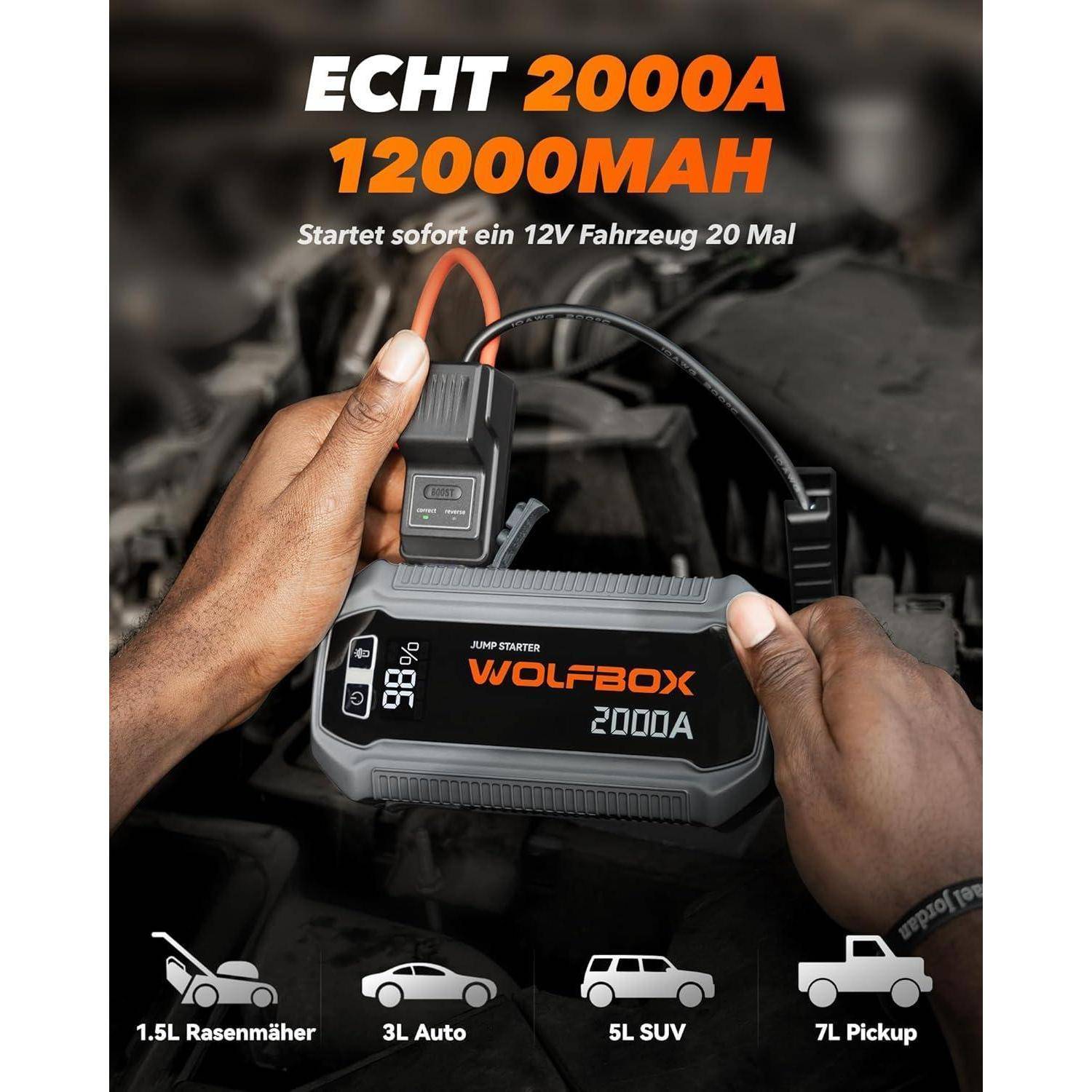 Hände halten ein WOLFBOX 2000A-Starthilfegerät mit Kabeln in einem Automotorraum; der Anzeigentext sagt „ECHT 2000A 12000MAH