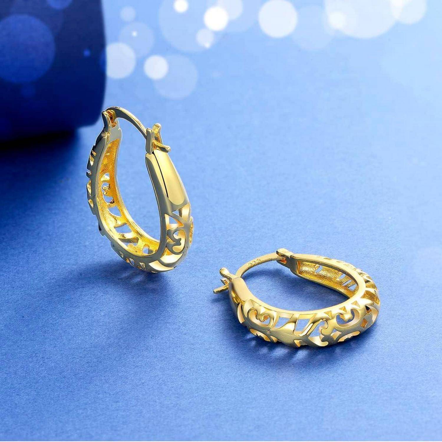 Zwei goldene Creolen mit ornamentalem Durchbruchdesign auf einer blauen Oberfläche, eine aufrecht stehend und eine flach liegend.