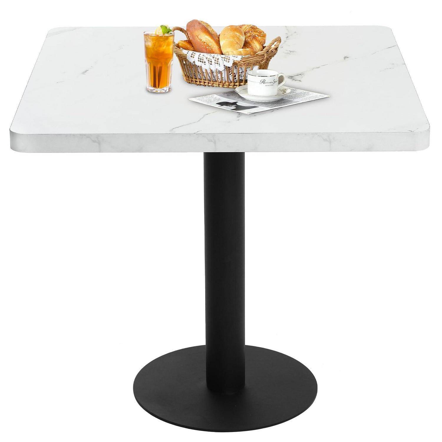 Quadratischer Café-Tisch mit weißem Marmor-Look und schwarzem Sockelfuß, eingedeckt mit einem Brotkorb, orangefarbenem Getränk und Kaffeetasse