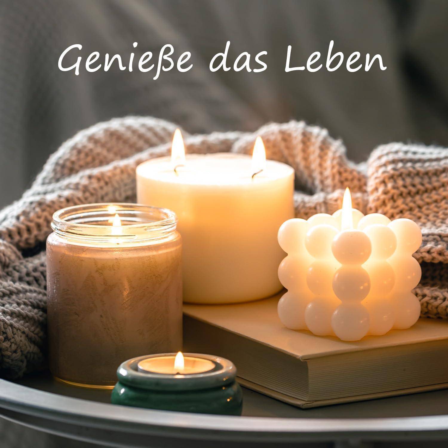 Stillleben mit brennenden Kerzen, einer Glaskerze, einer Blasenkerze auf einem Buch und einer gestrickten Decke; der Text liest sich „Genieße das Leben
