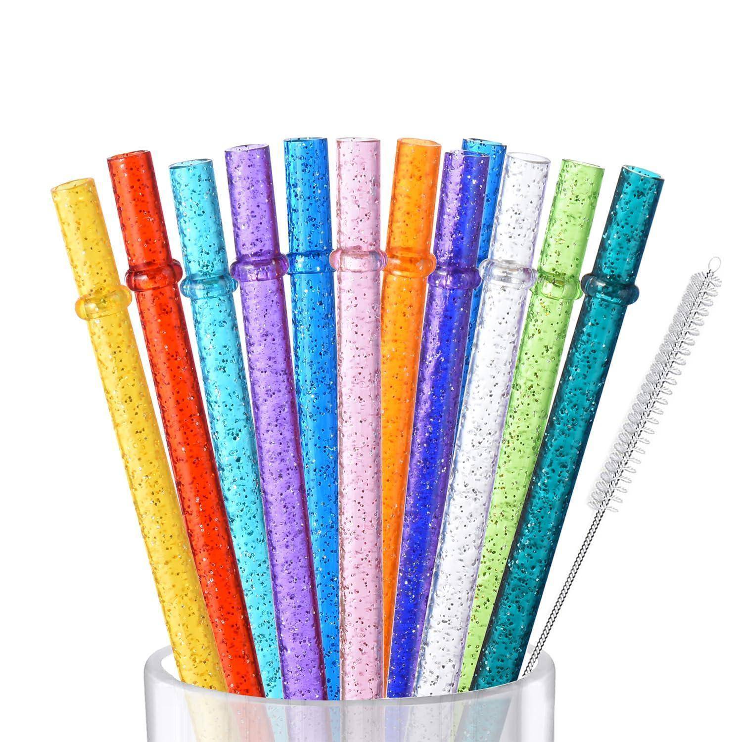 Bunte glitzernde Kunststoff-Trinkhalme in einem weißen Becher, daneben eine kleine weiße Reinigungsbürste.