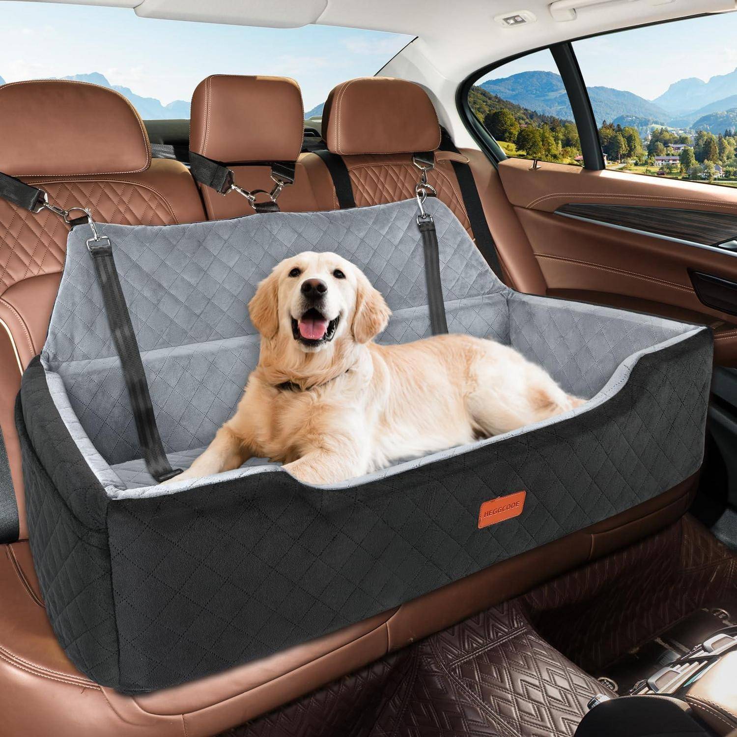 Golden Retriever, der in einer grauen Autositz-Hängematte für Haustiere auf der Rückbank eines Autos liegt, mit Bergen, die außerhalb des Fensters sichtbar sind.