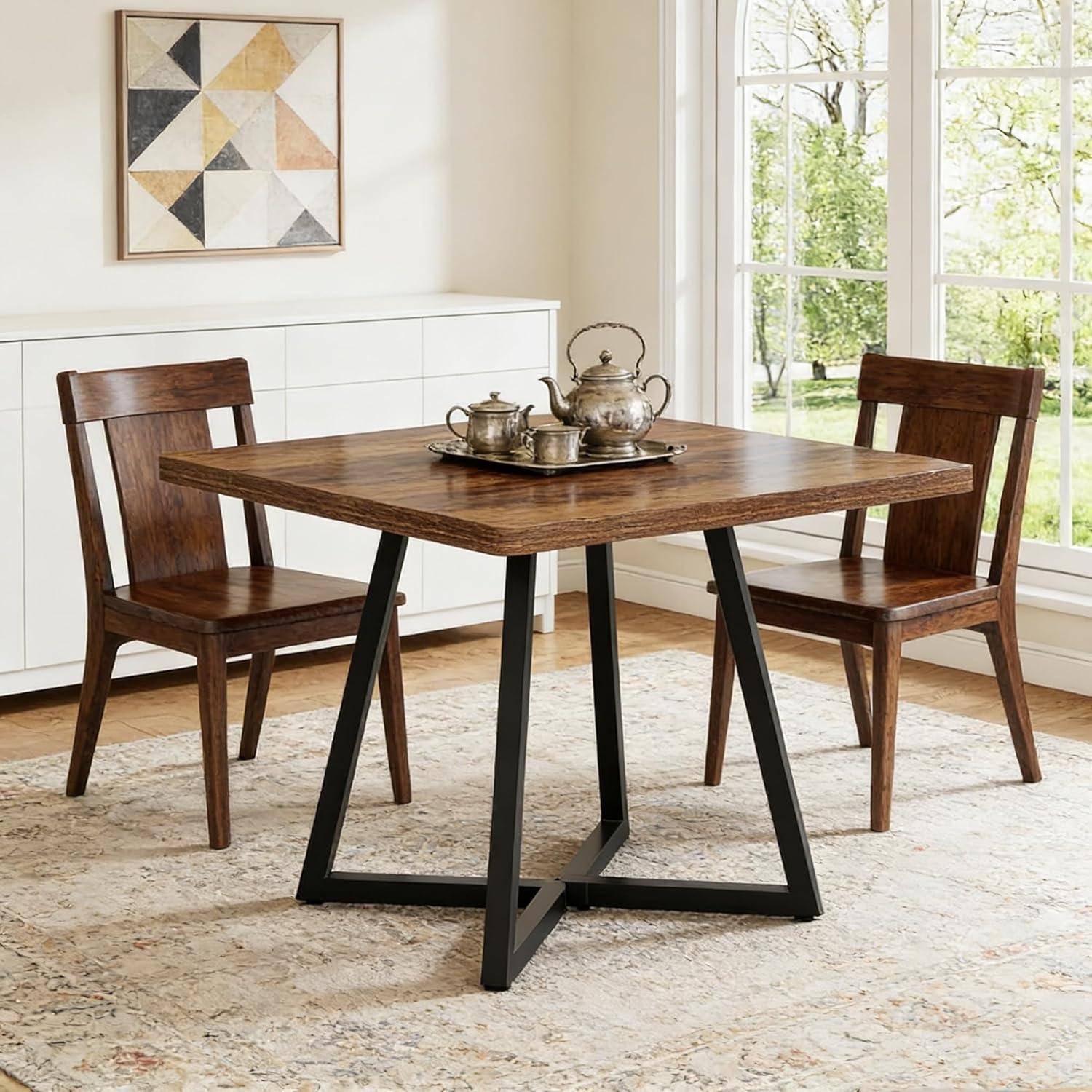 Modernes Esszimmerset mit quadratischem Holztisch, schwarzem Metallgestell, zwei Holzstühlen und Teeservice in einem hellen Raum neben großen Fenstern.