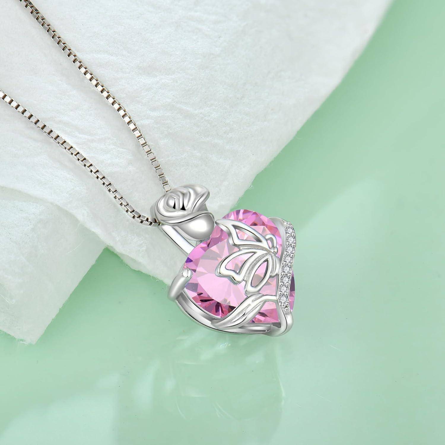 Silberne Anhängerkette mit großem rosa herzförmigem Edelstein und Schmetterlingsdesign an einer Kette, gezeigt auf hellgrünem Hintergrund.